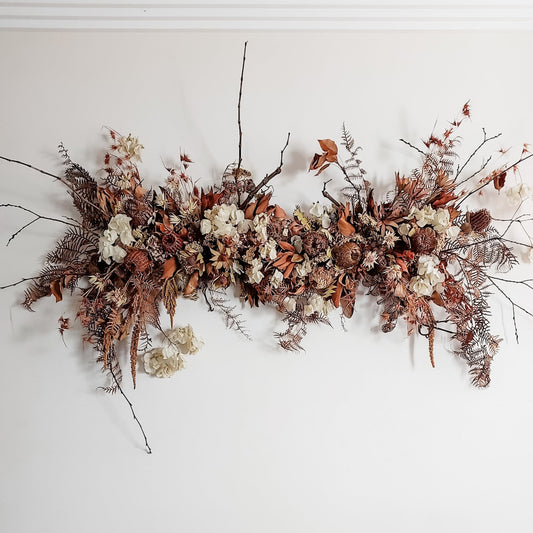 Wall installation of dried florals in earthy, rust tones.