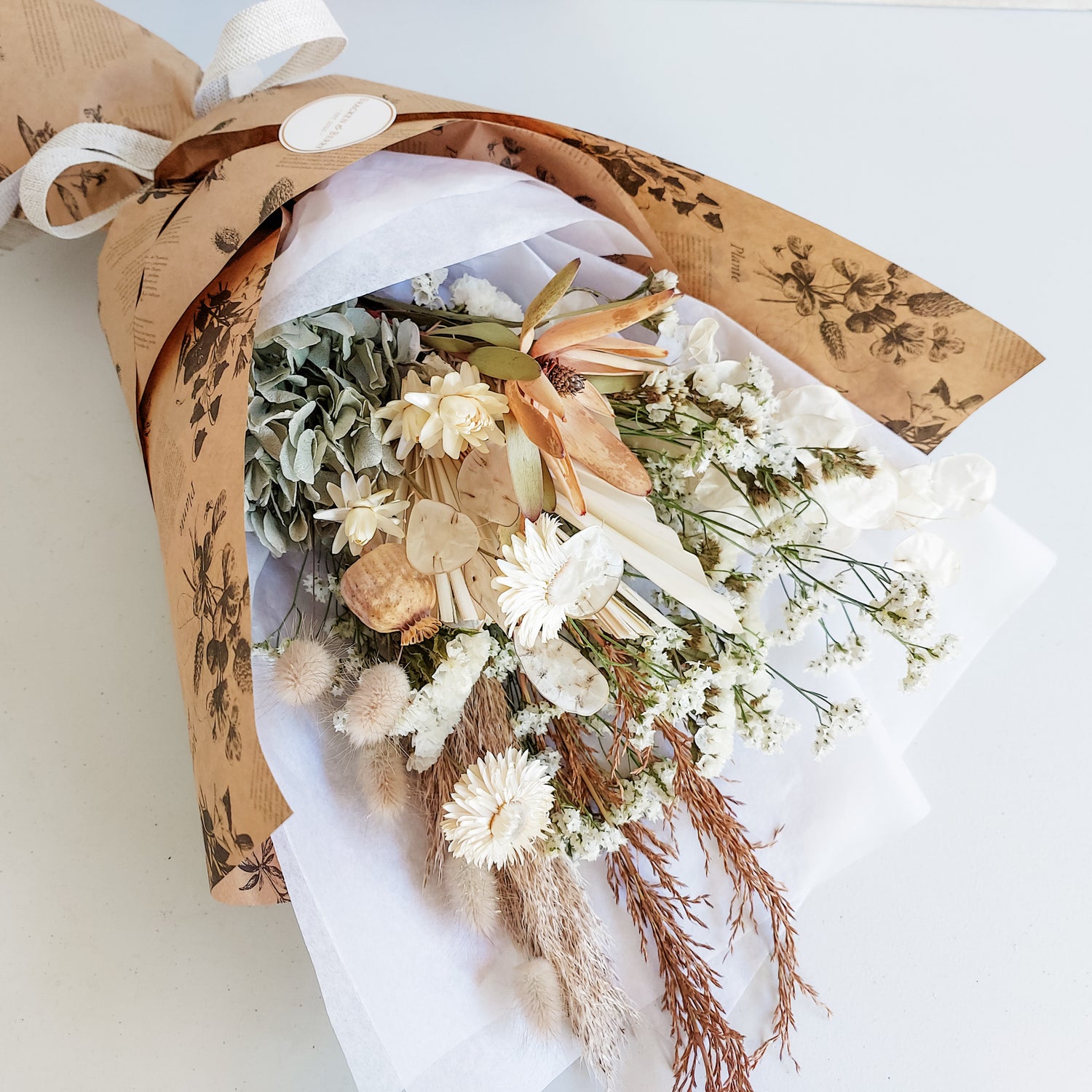 Dried flower bouquet in soft blue and neutral tones wrapped ready for gifting.