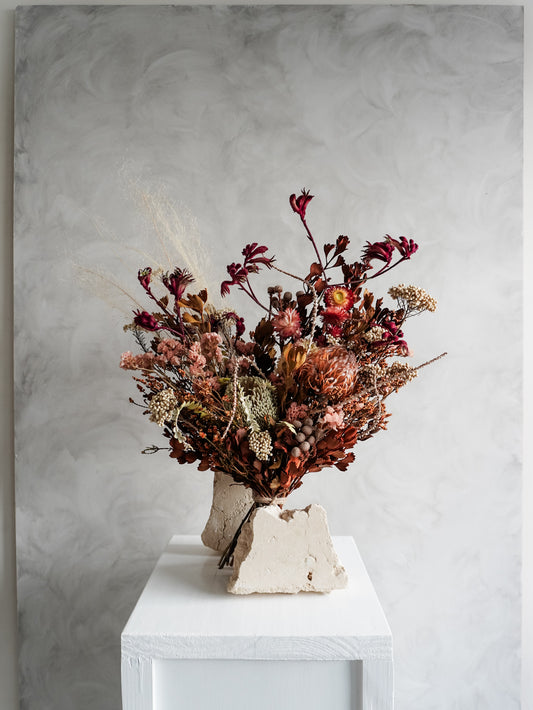 Bouquet of autumnal dried flowers on a white plinth with a grey background - luxe size distant view.