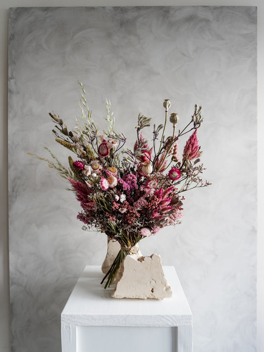 Bouquet of colourful dried flowers on a white plinth against a grey background - luxe size distant view.