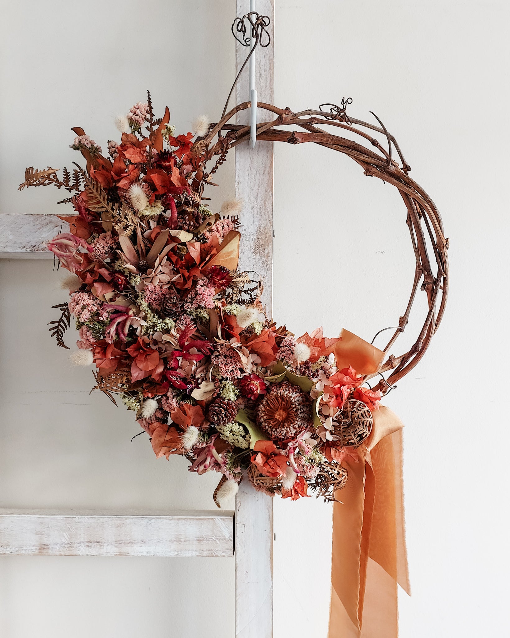 Dried flower wreath in deep red tones with native flowers on a grapevine base.