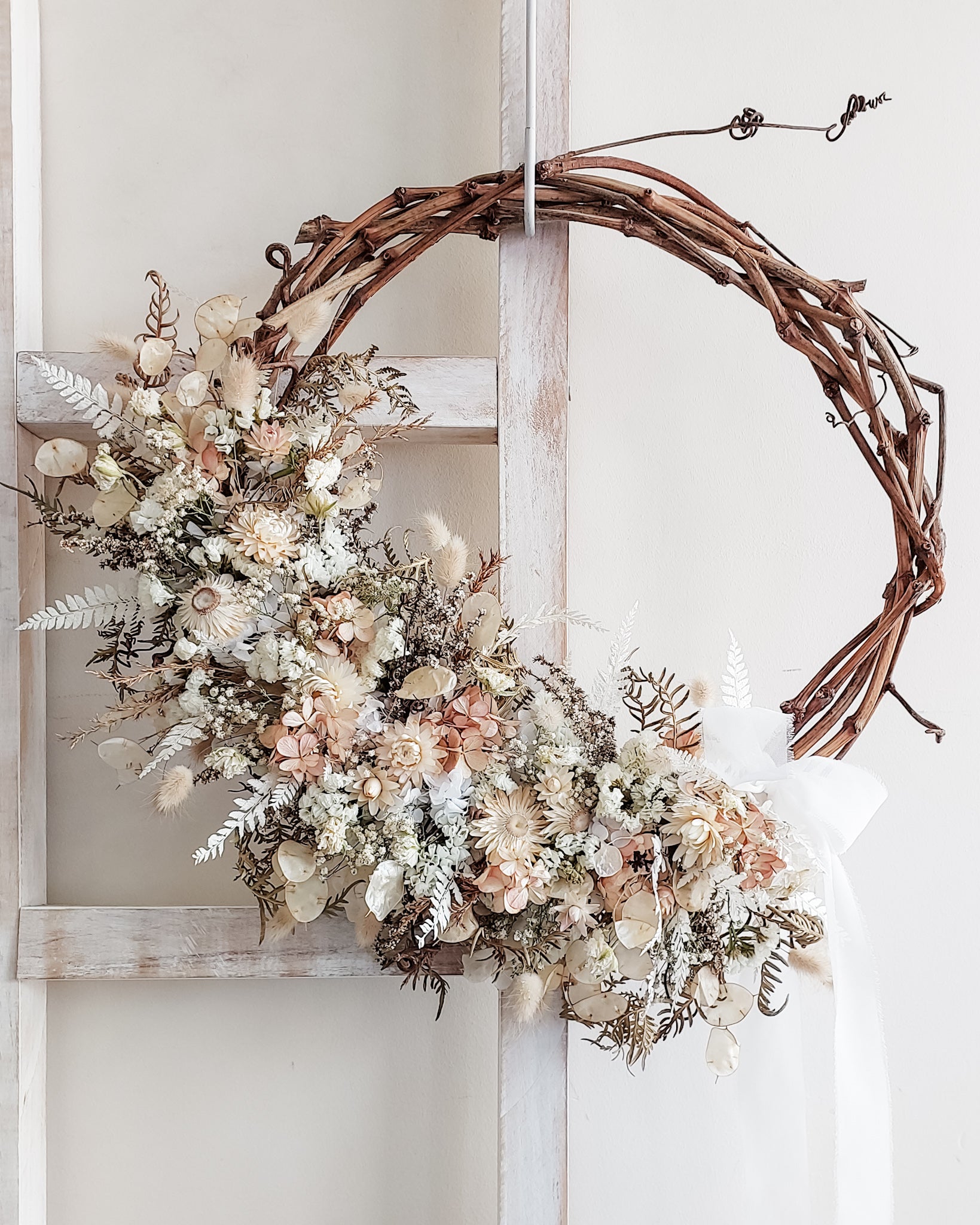 Dried flower wreath in white and 
blush tones on a grapevine base.