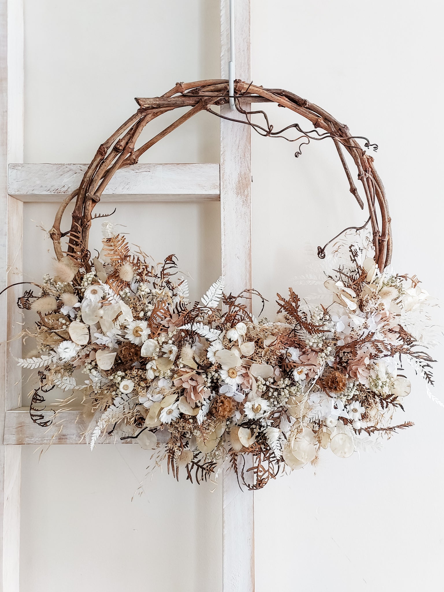 Dried flower wreath in neutral white tones on a grapevine base.