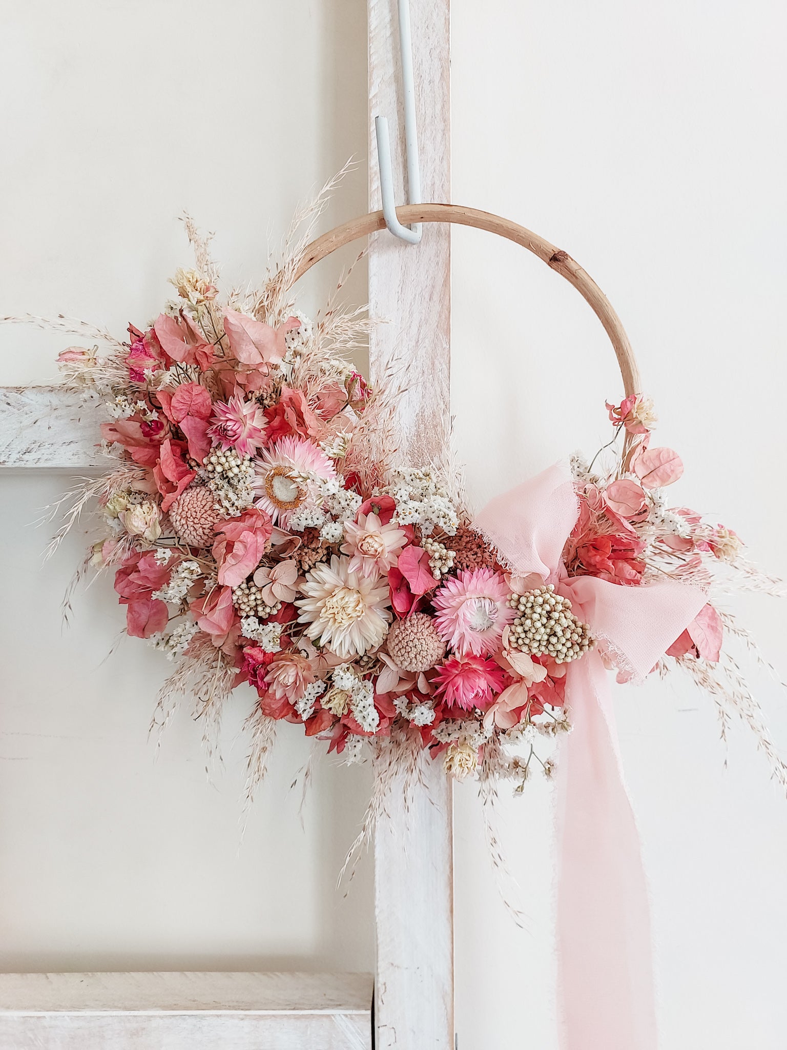 Dried flower wreath in soft pink tones on a small rattan hoop with lush pink ribbon.