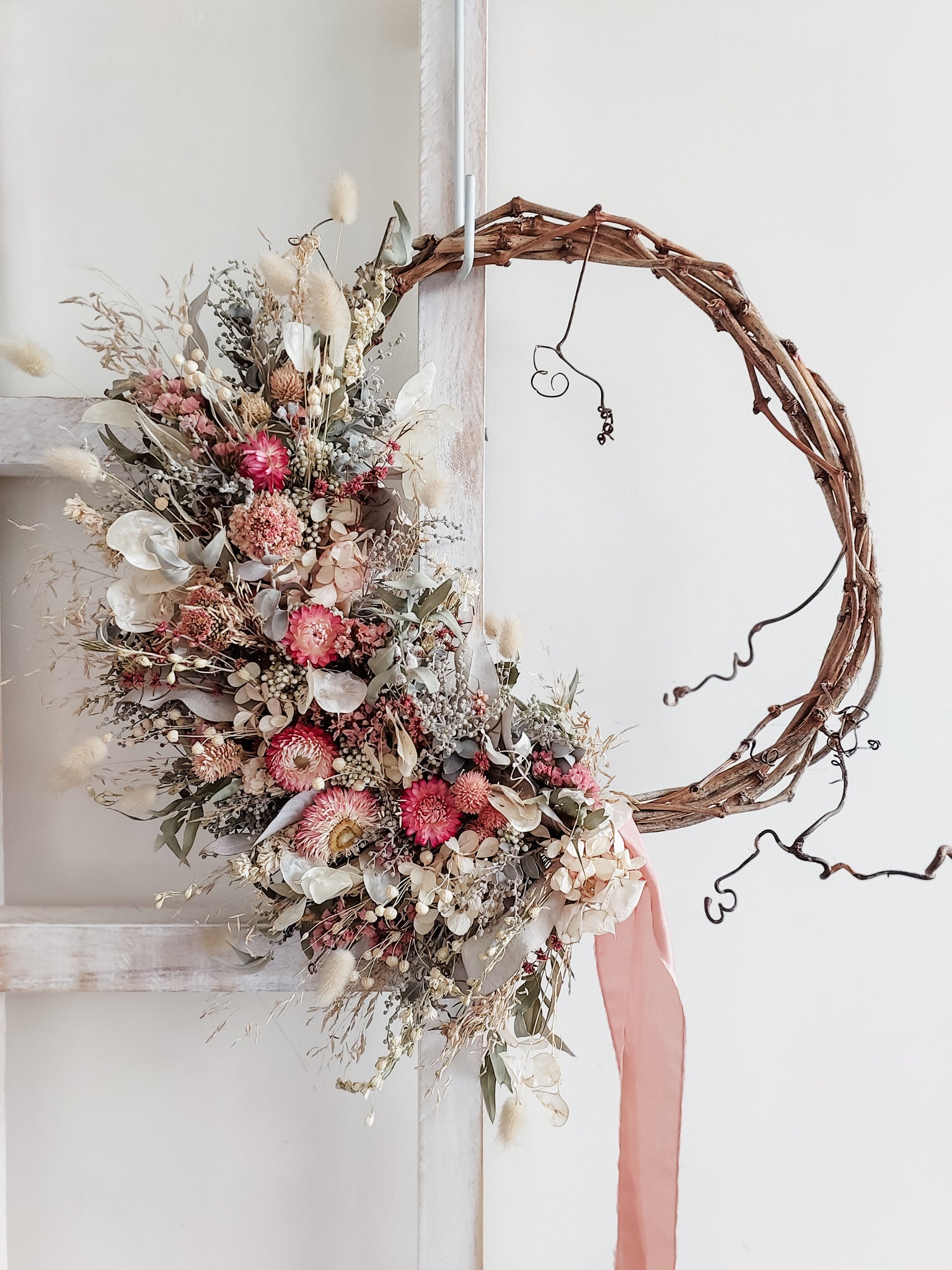 Dried flower wreath in pastel pink tones on a grapevine base.