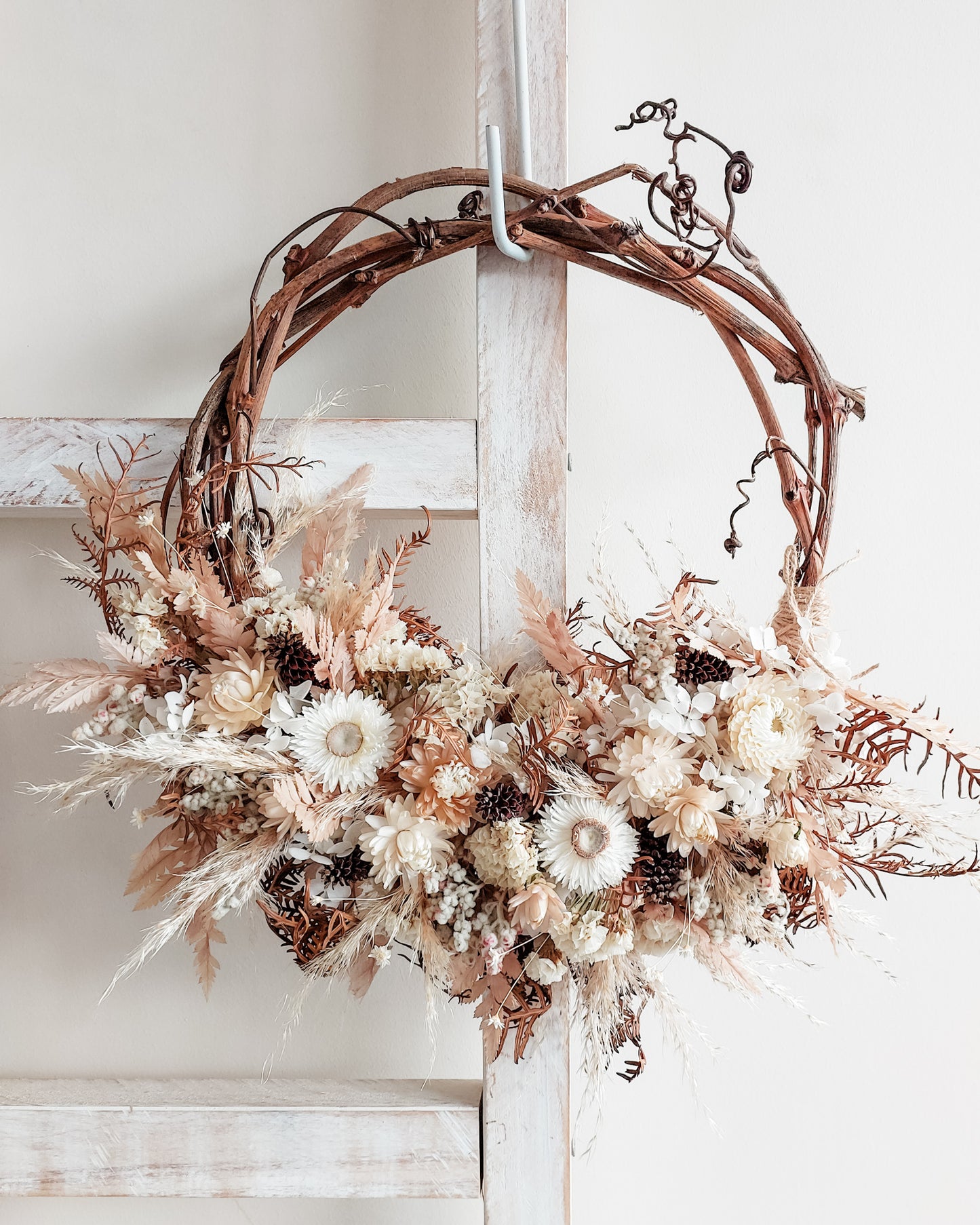 Dried flower wreath in soft white and neutral tones on a grapevine base.