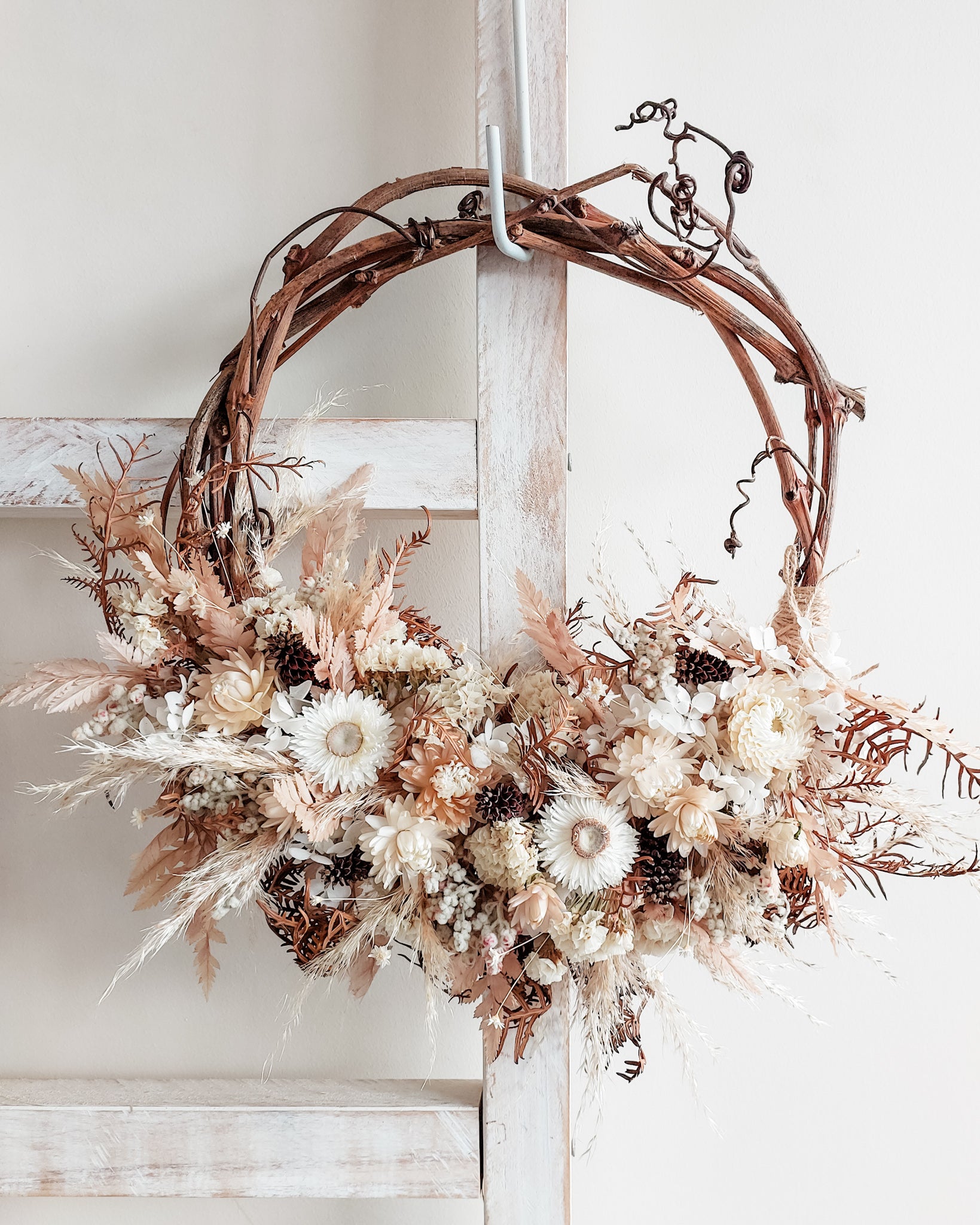 Dried flower wreath in soft white and neutral tones on a grapevine base.