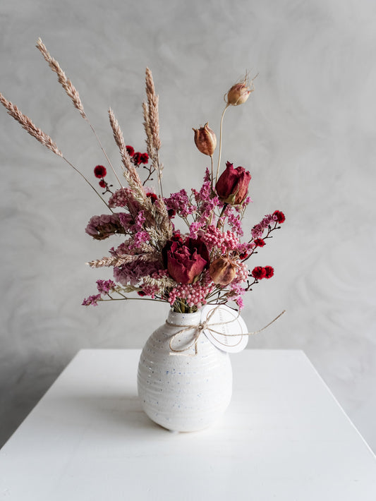 Dried flower arrangement in ceramic bud vase with pink and red florals – close view.