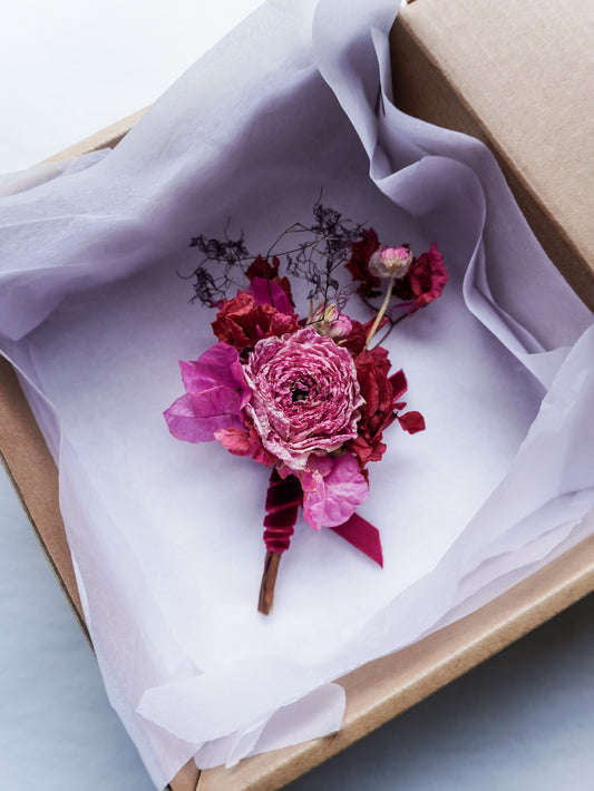 Dried pink floral boutonniere in a box with white tissue paper.