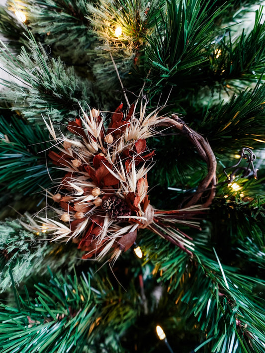Dried flower mini wreath decoration in earthy tones on a grapevine base hung on a green Christmas tree.
