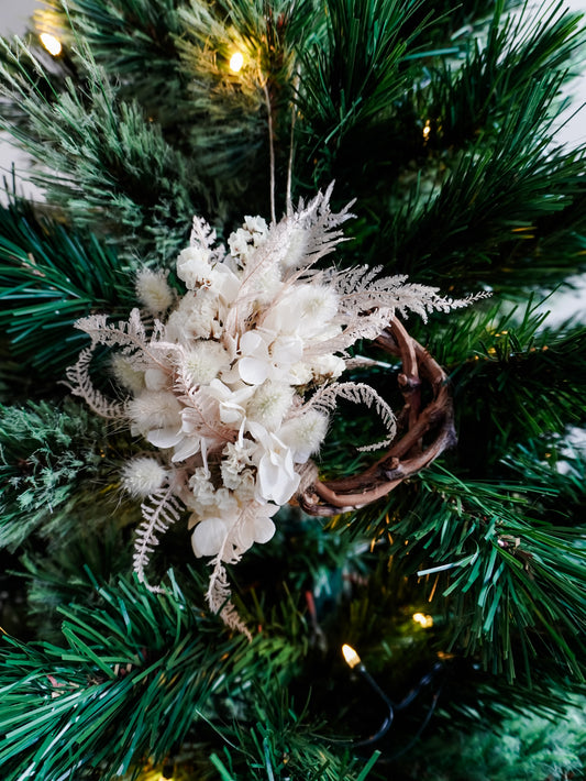 Dried flower mini wreath decoration in soft pink and white tones on a grapevine base hung on a green Christmas tree.