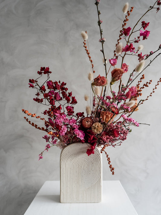 Dried flower arrangement in bold pink and red tones in a ceramic vessel – close view.