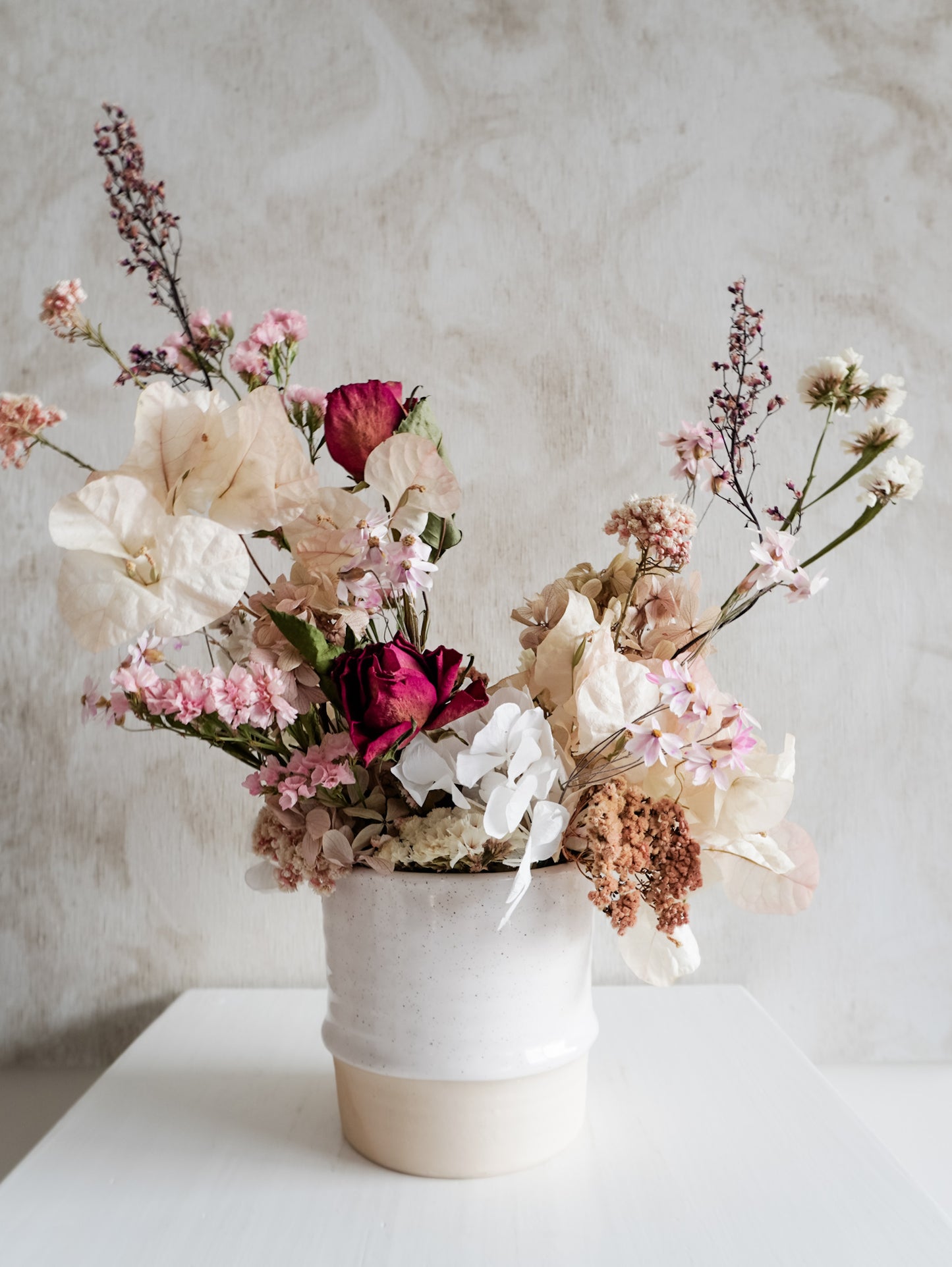 Dried flower arrangement in ceramic vessel with pastel florals and deep pink roses – close view.