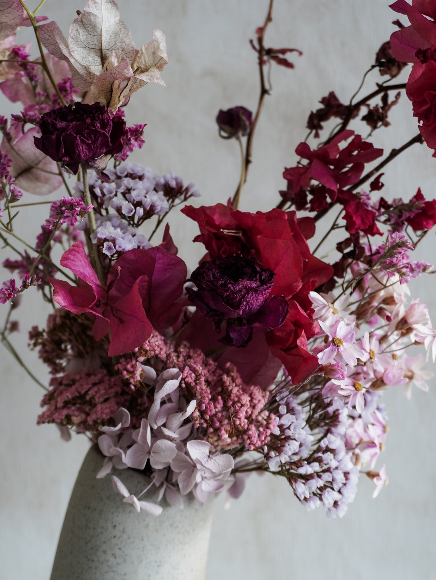 Dried flower arrangement in ceramic vase with deep pink florals – close up view.