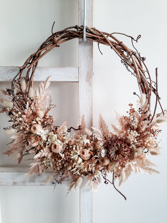 Dried flower wreath in blush and neutral tones on a grapevine base.
