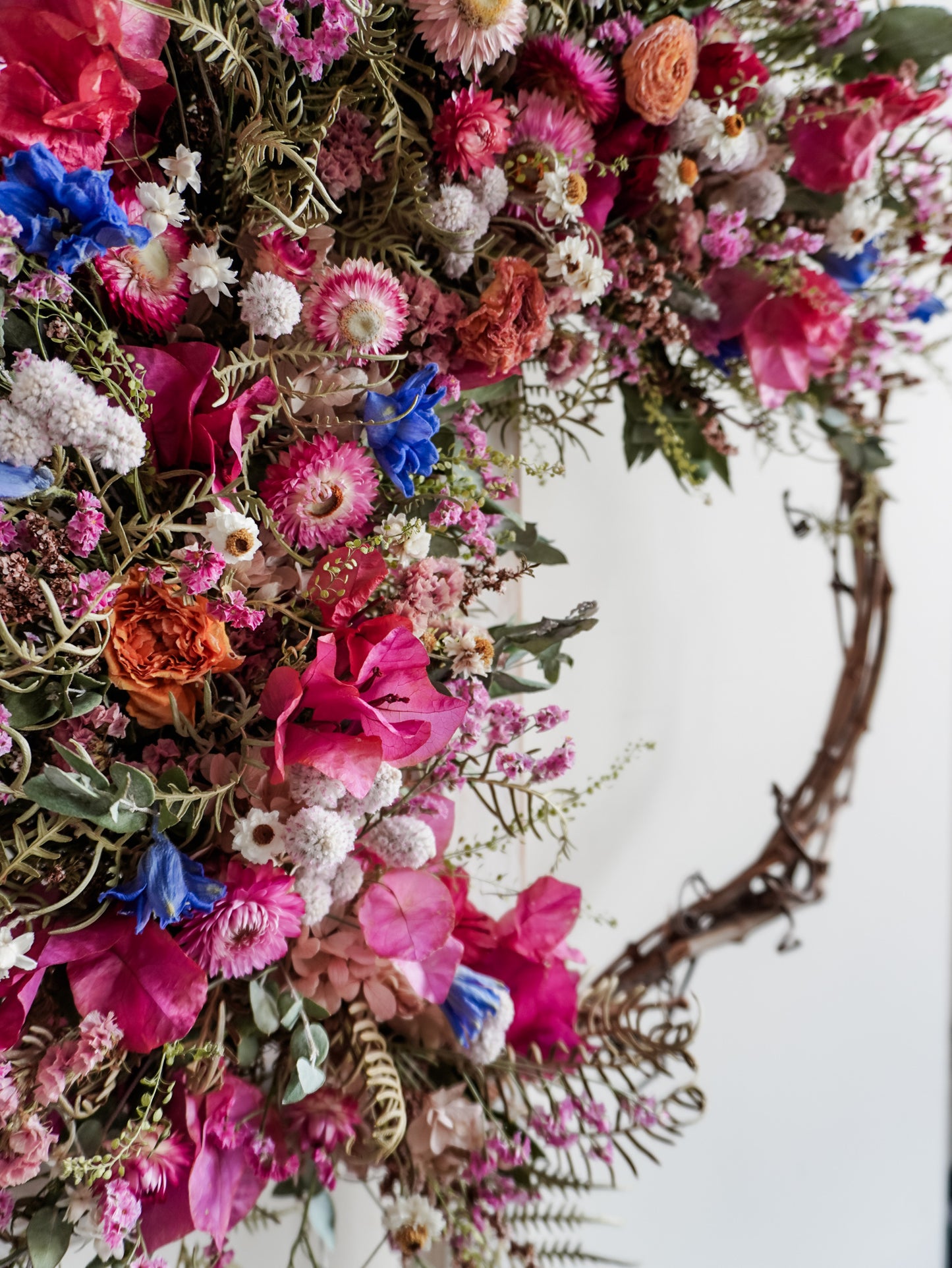 Dried flower wreath in bright, colourful tones with spring florals on a grapevine base – close up view.
