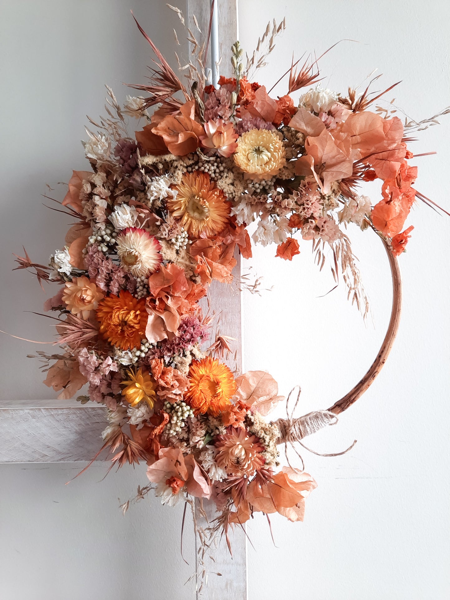 Dried flower wreath in sunset tones on a small rattan hoop.