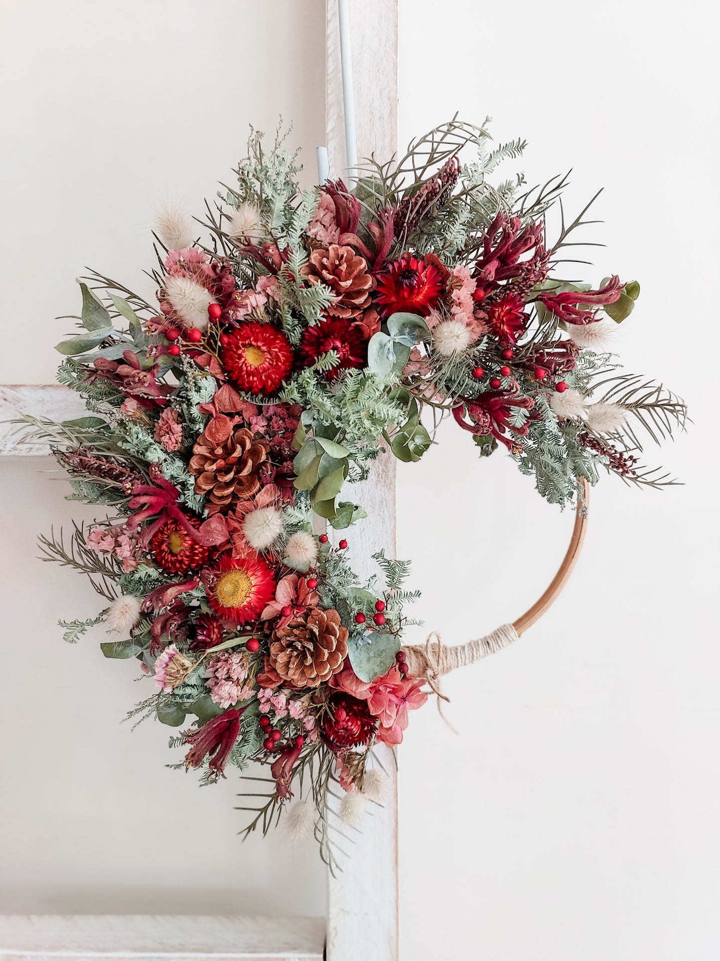 Dried flower wreath in festive colours on a small rattan hoop.
