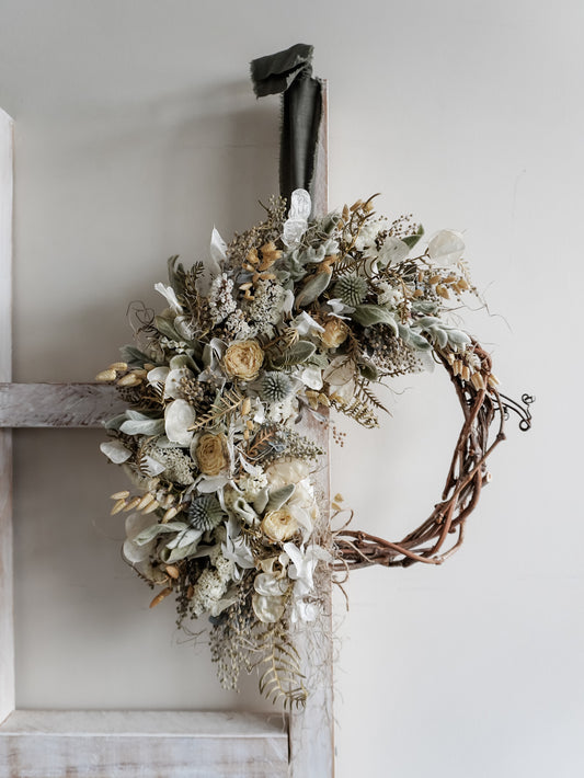 Decorative wreath with dried flowers and leaves on a white wall.