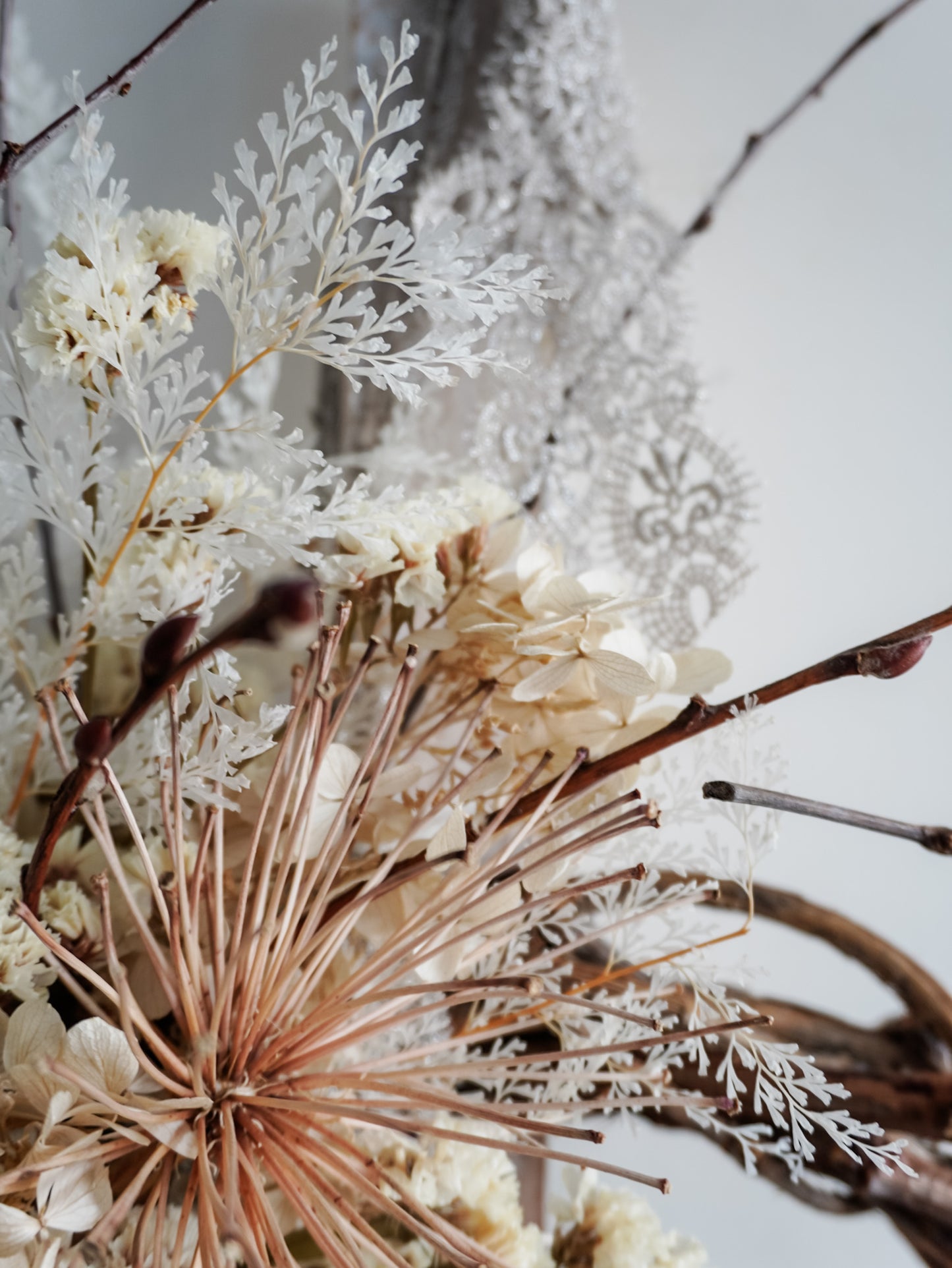 Dried flower wreath in nude neutral tones spray design on a grapevine base – close up of fern and lace.