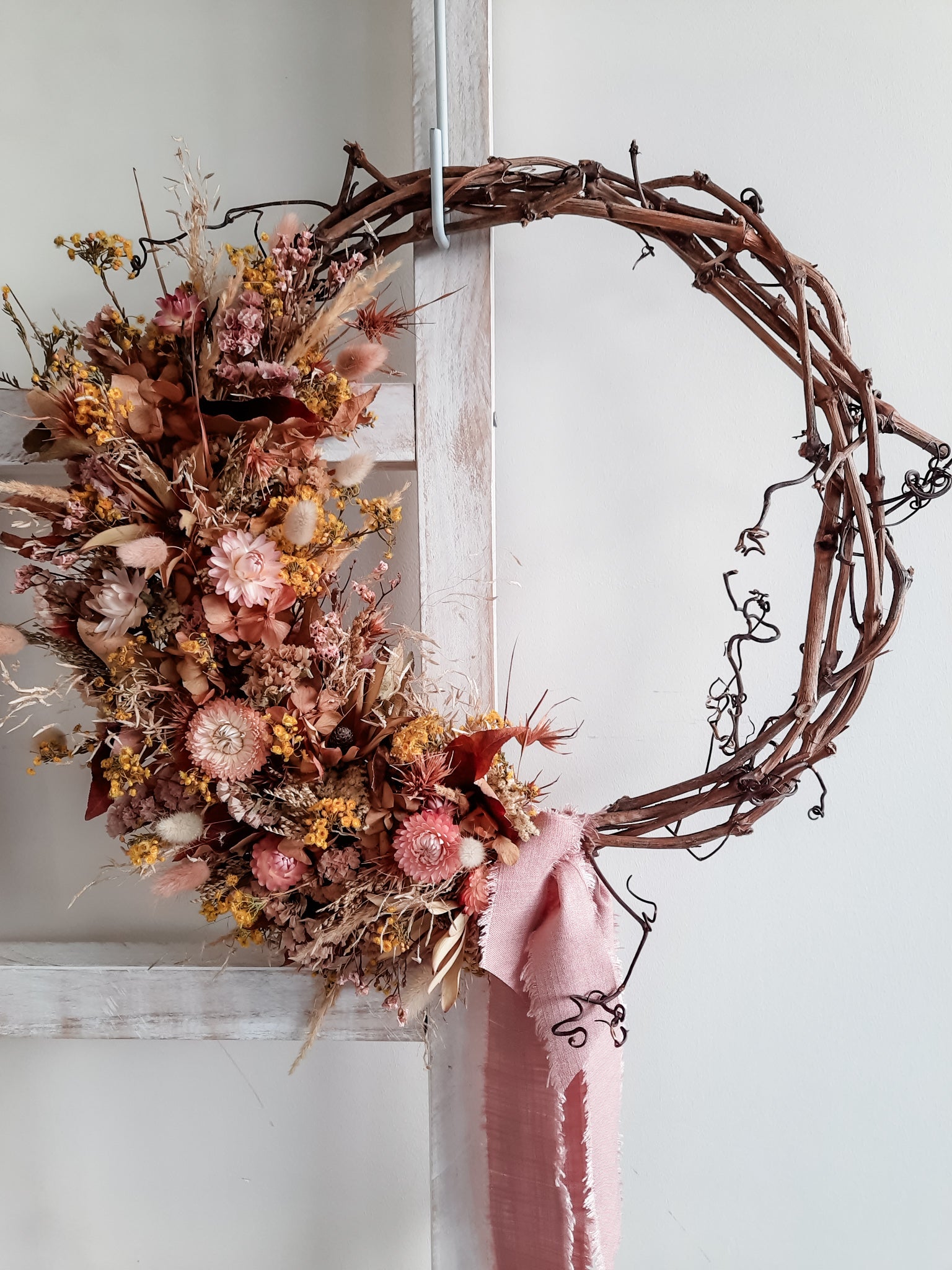 Dried flower wreath in warm tropical tones on a grapevine base.