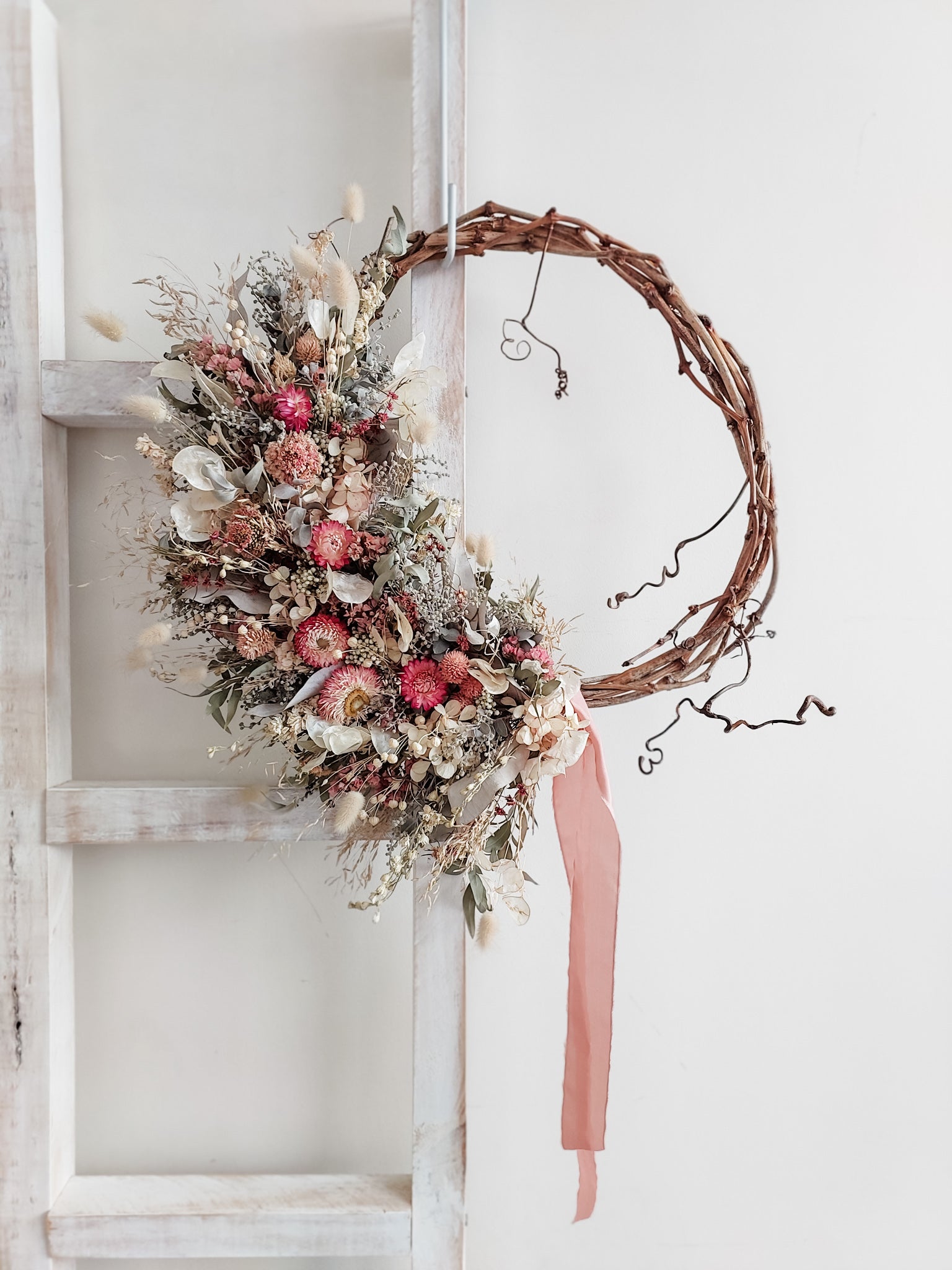 Dried flower wreath in a rustic style in pink and green tones on a grapevine base – distant view.