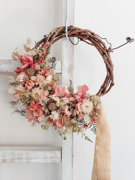 Dried flower wreath in soft pastel tones on a grapevine base.