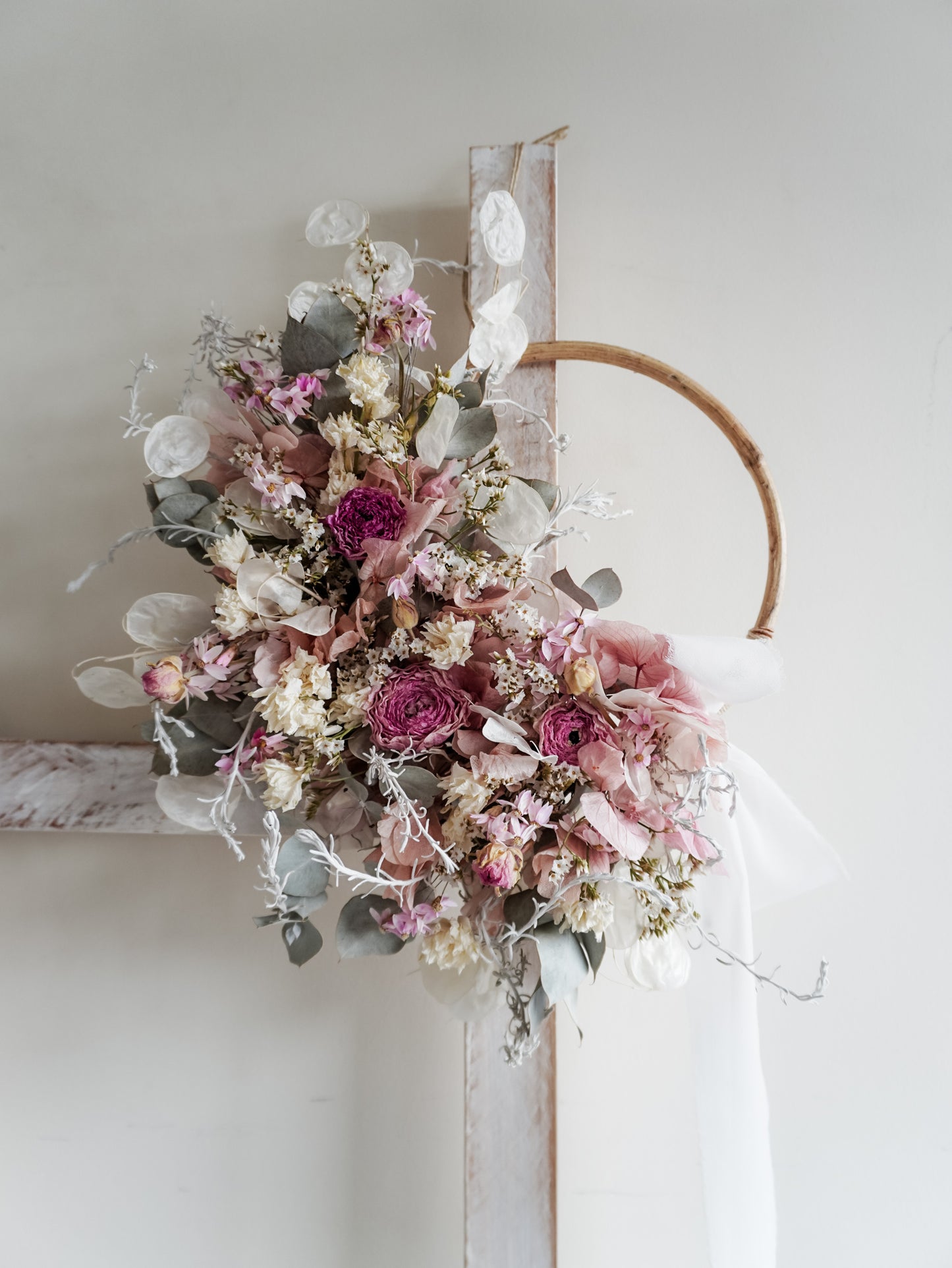 Dried flower wreath in soft pastel tones on a rattan hoop base with white ribbon - close view.