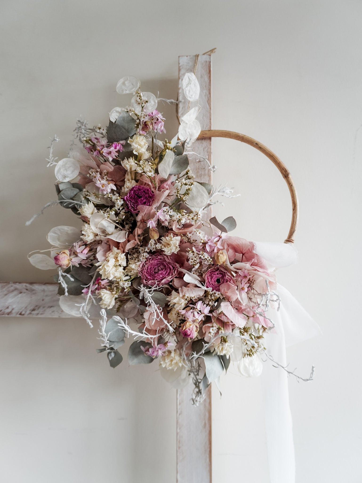 Dried flower wreath in soft pastel tones on a rattan hoop base with white ribbon - close view.