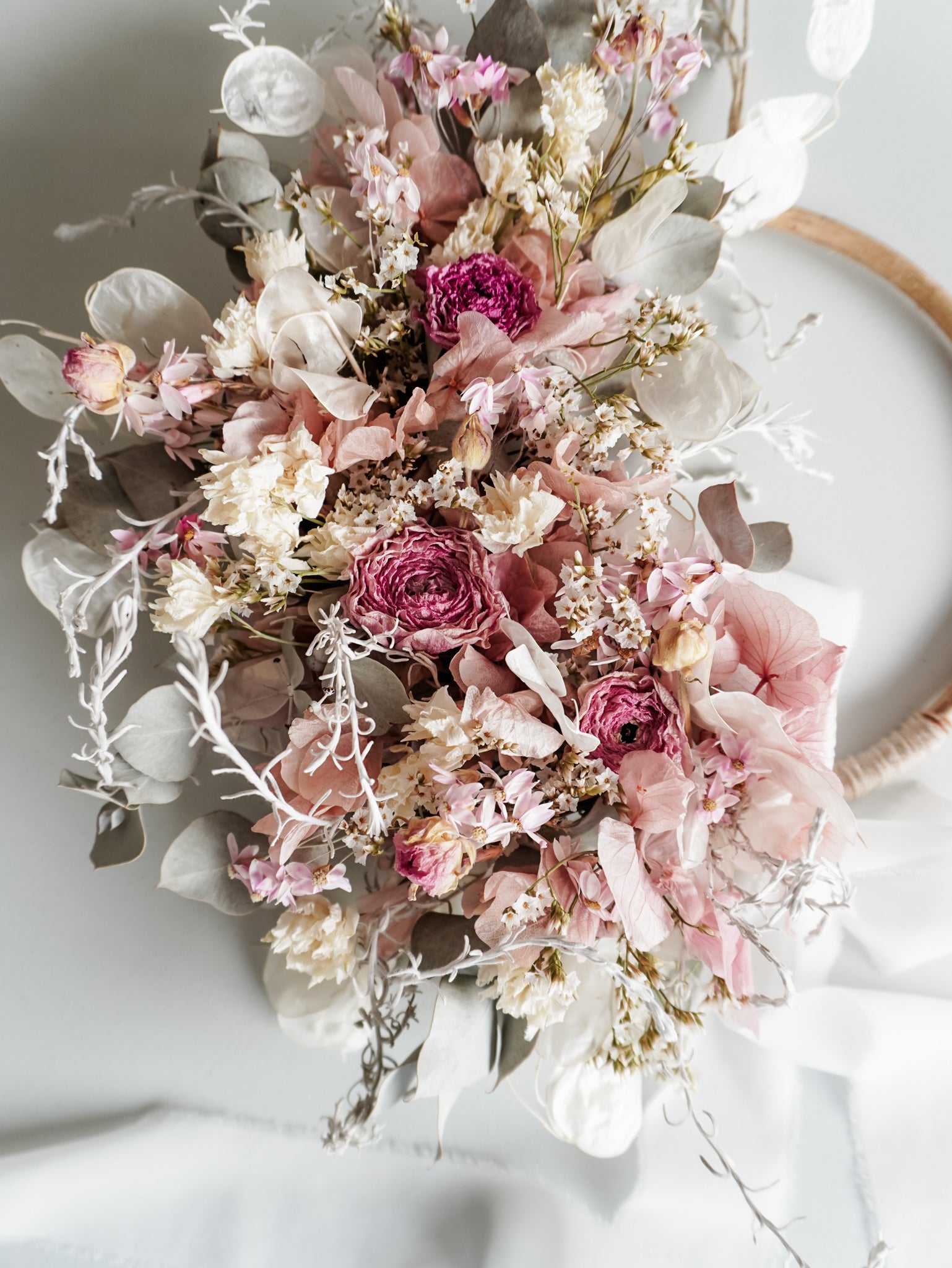 Dried flower wreath in soft pastel tones on a rattan hoop base with white ribbon - aerial view.