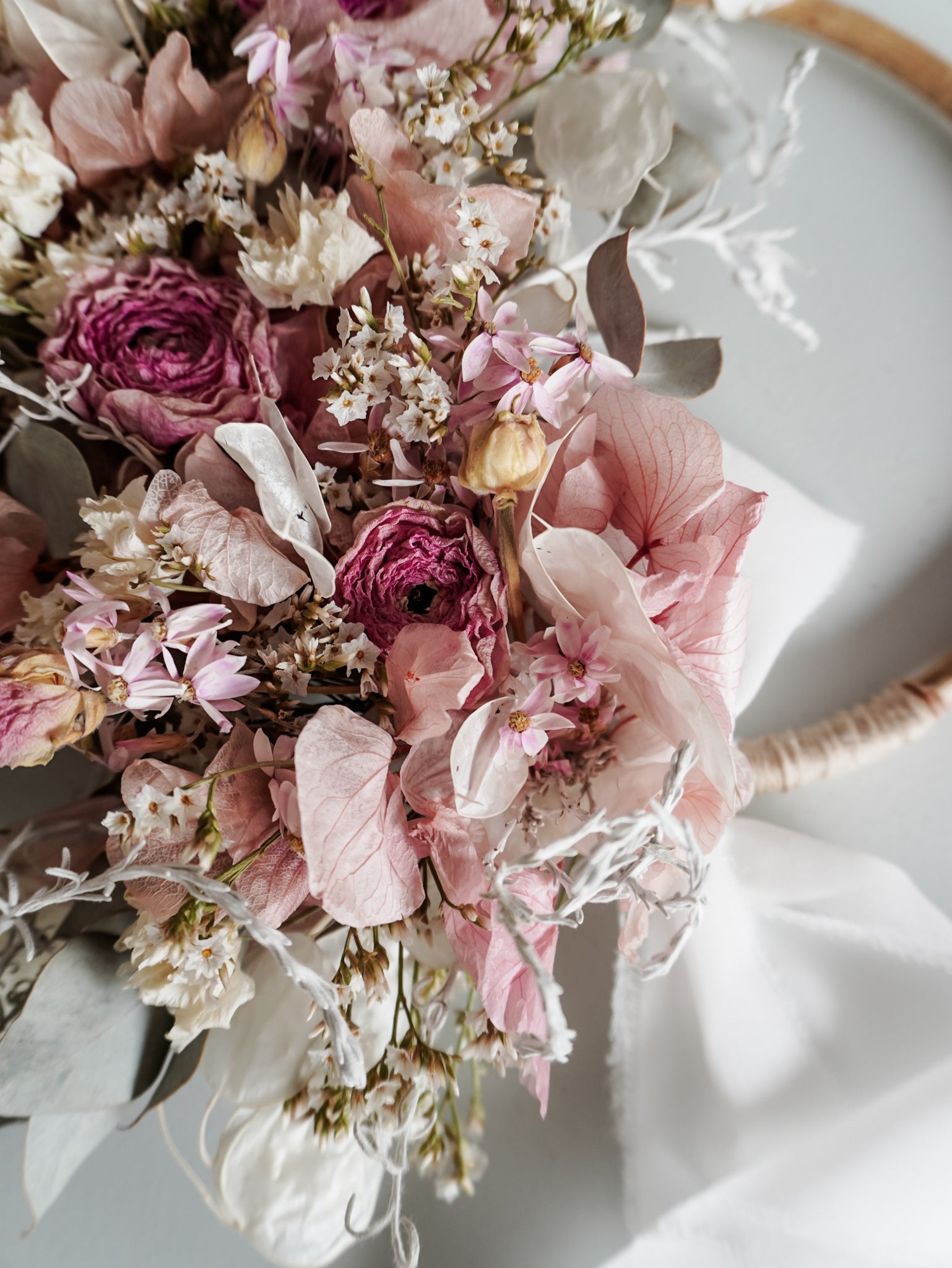 Dried flower wreath in soft pastel tones on a rattan hoop base with white ribbon - close up view.