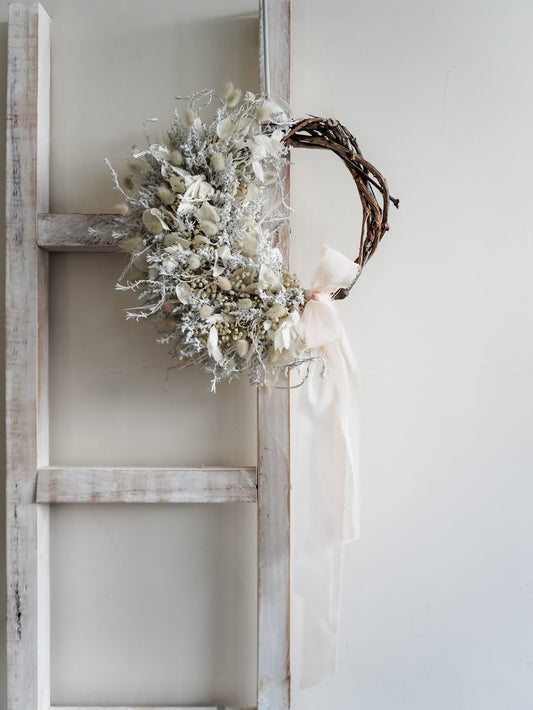 Dried flower wreath in classic white Christmas inspired tones on a grapevine base – distant full view.
