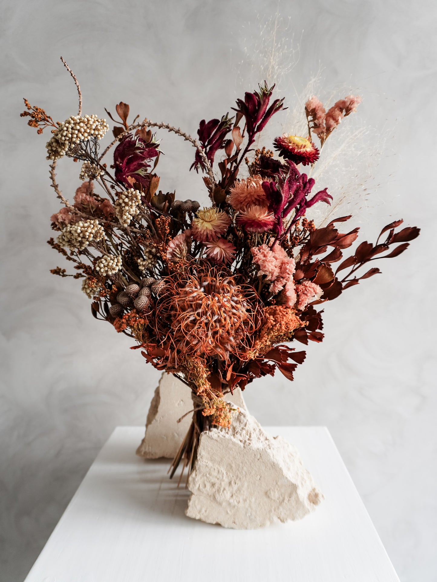 Bouquet of autumnal dried flowers on a white plinth with a grey background - classic size close view.