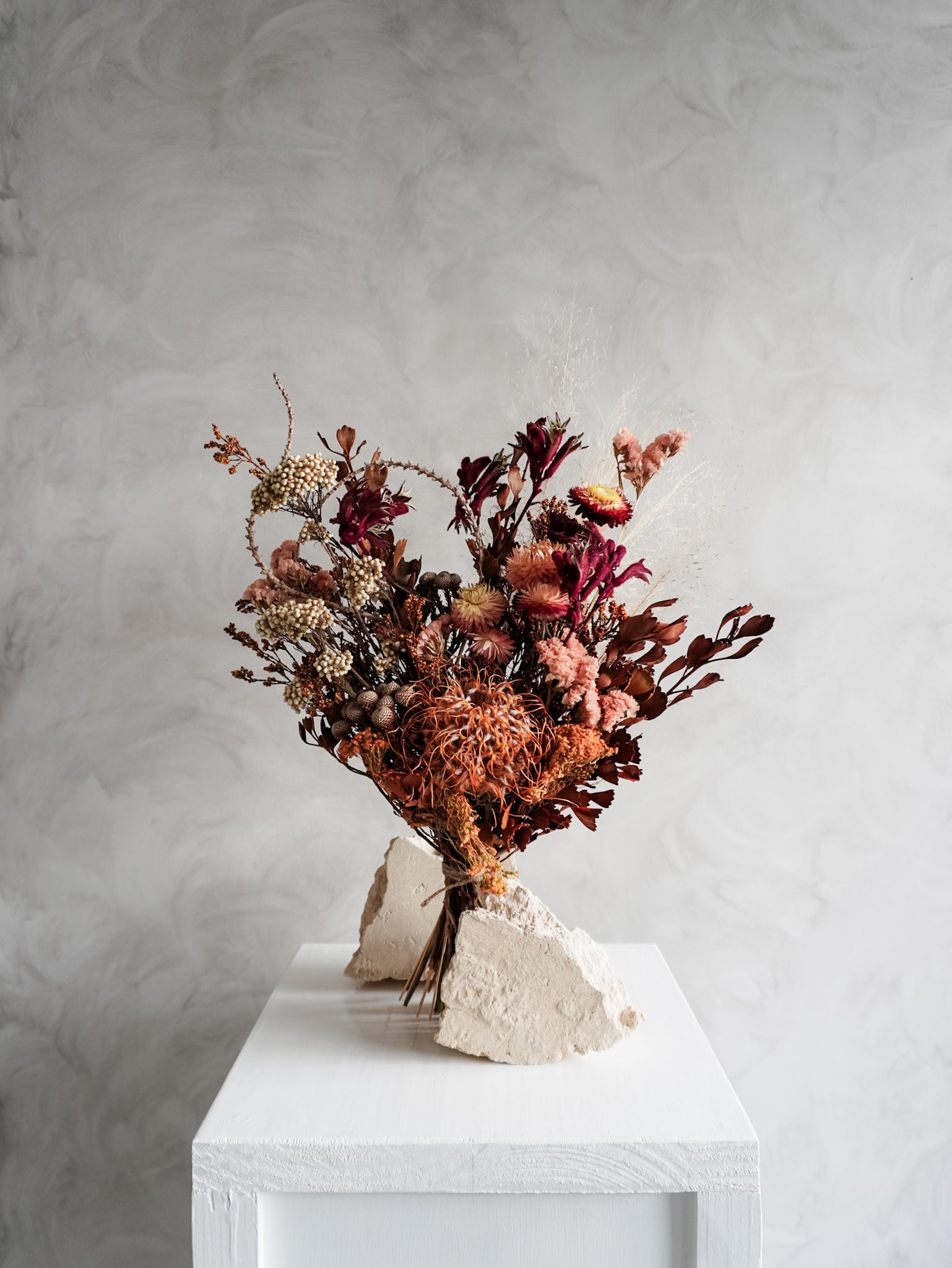 Bouquet of autumnal dried flowers on a white plinth with a grey background - classic size distant view.