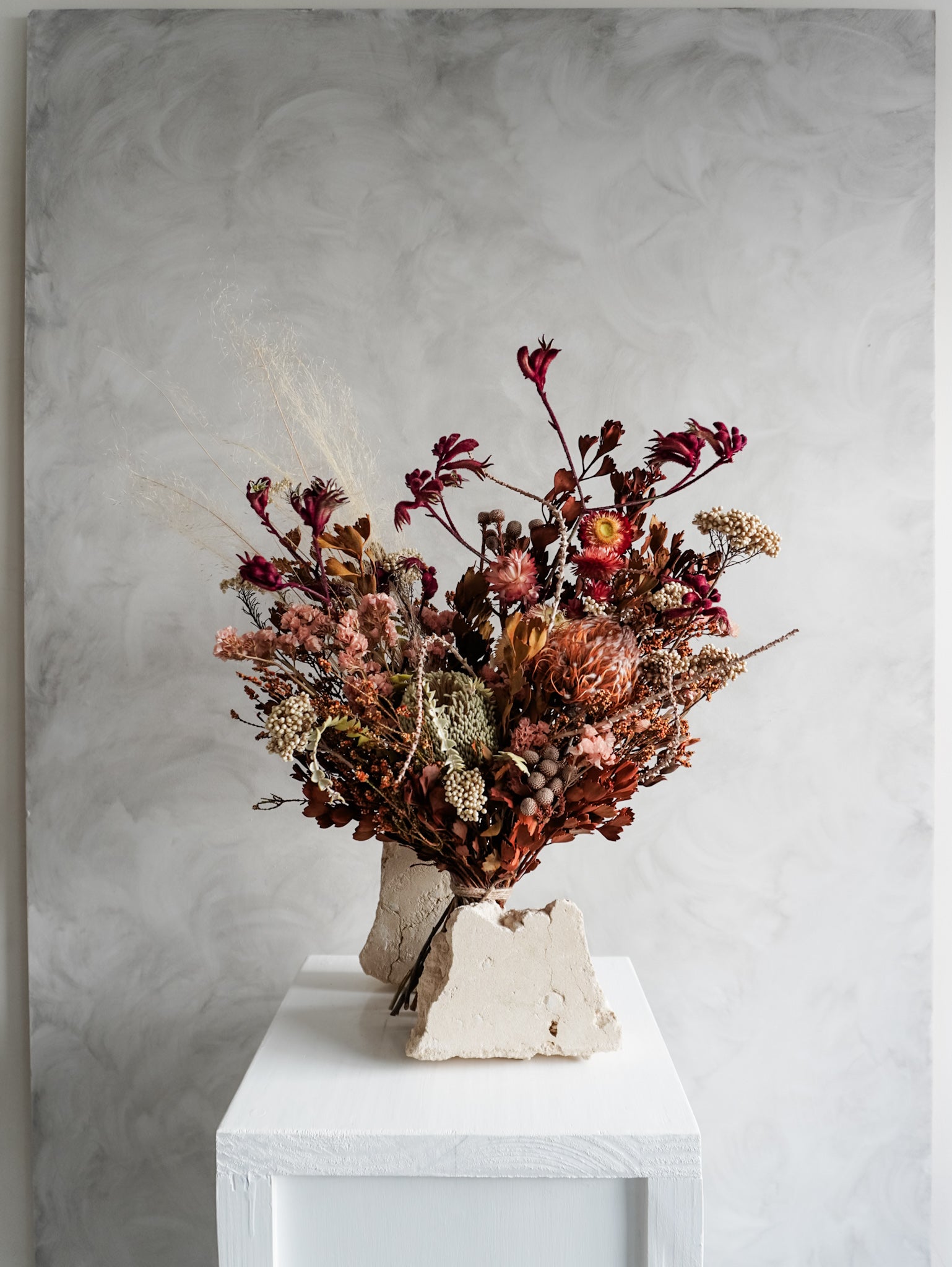 Bouquet of autumnal dried flowers on a white plinth with a grey background - luxe size distant view.