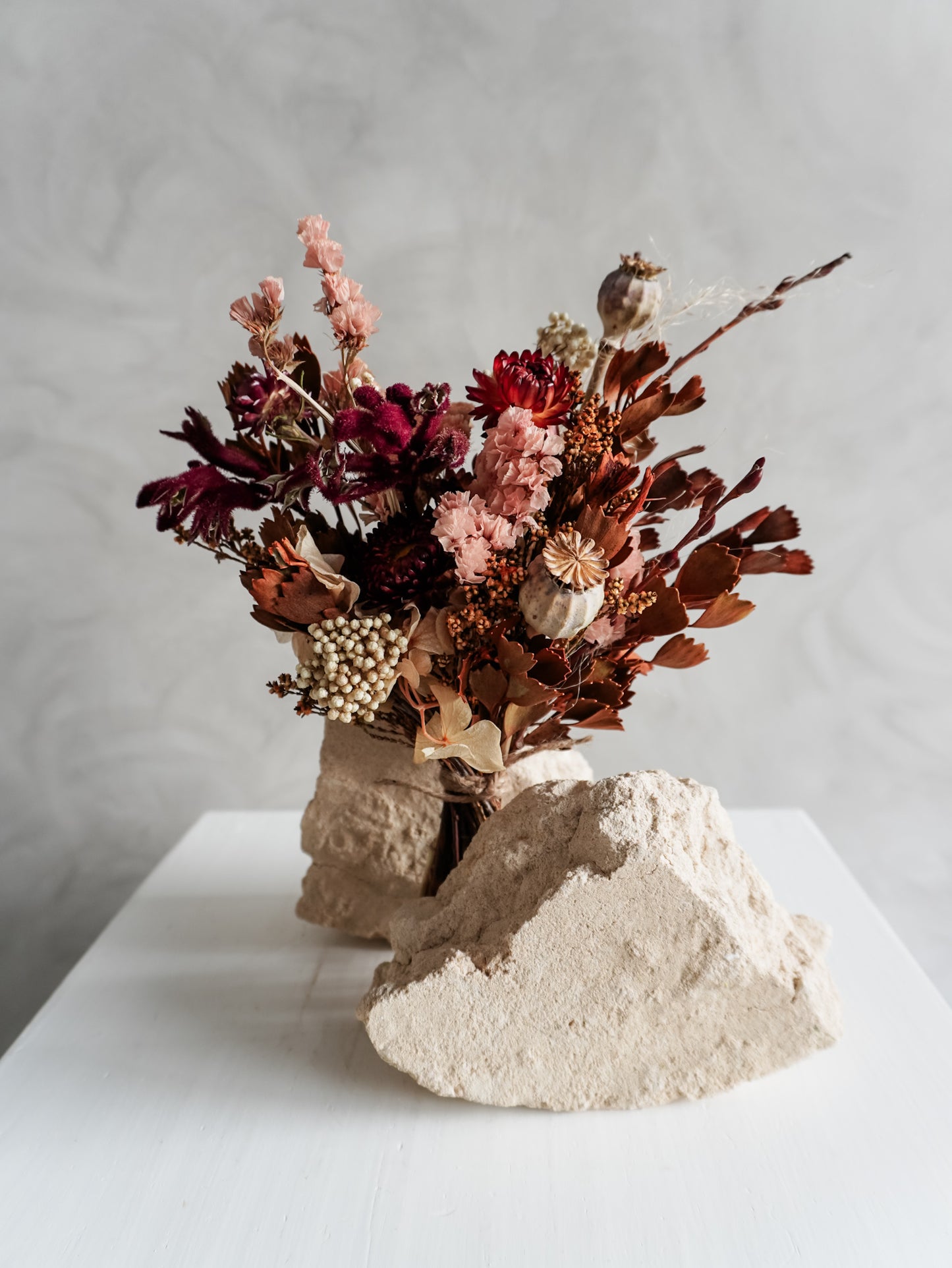 Bouquet of autumnal dried flowers on a white plinth with a grey background - posy size close view.