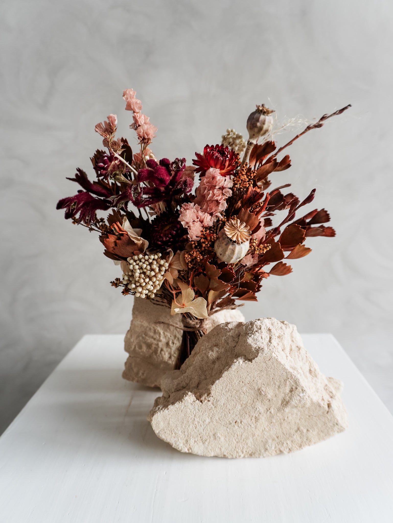 Bouquet of autumnal dried flowers on a white plinth with a grey background - posy size close view.