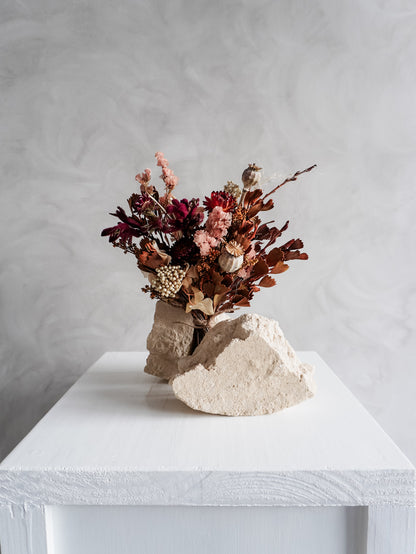 Bouquet of autumnal dried flowers on a white plinth with a grey background - posy size distant view.