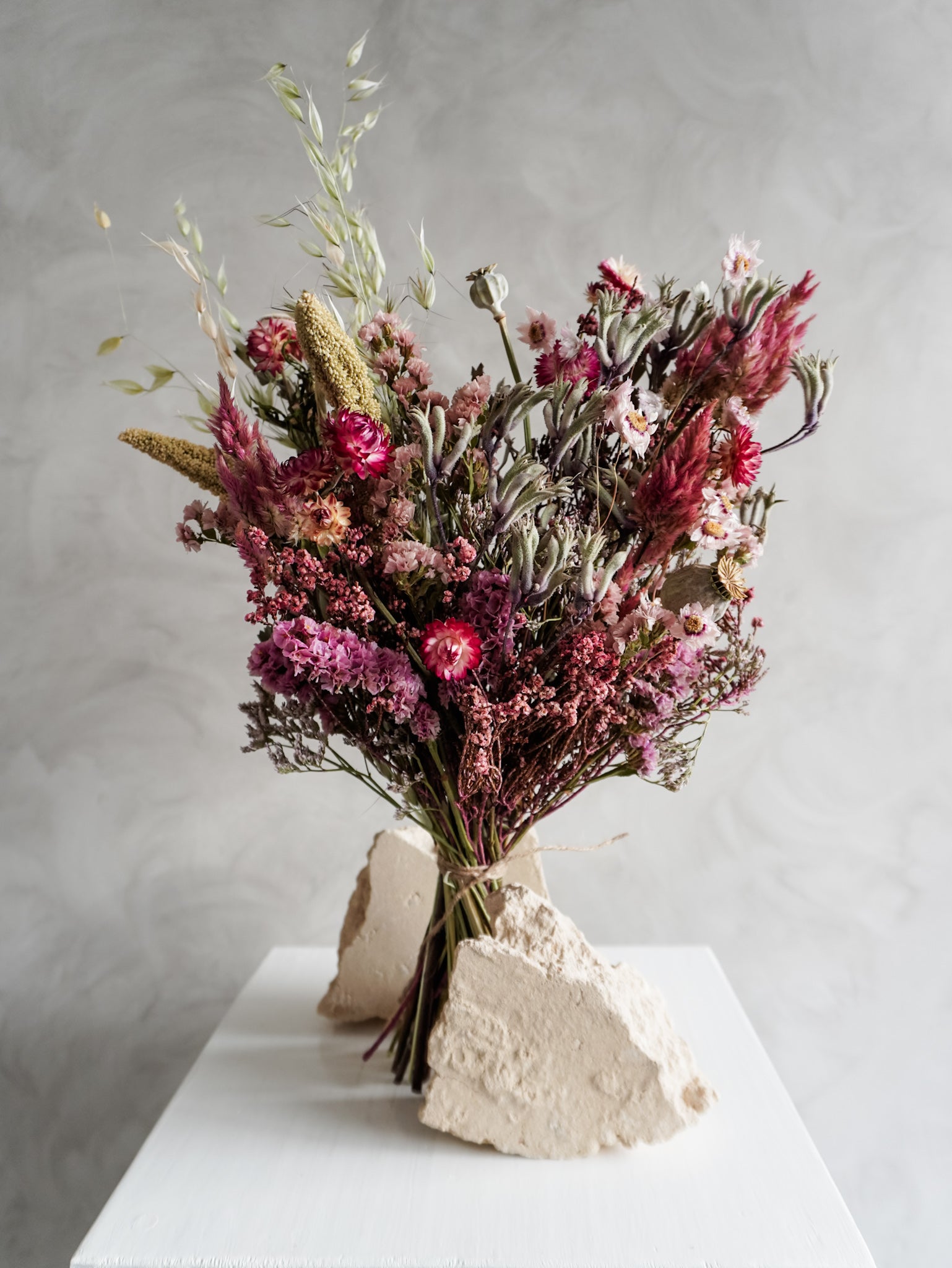 Bouquet of colourful dried flowers on a white plinth against a grey background - classic size close view.