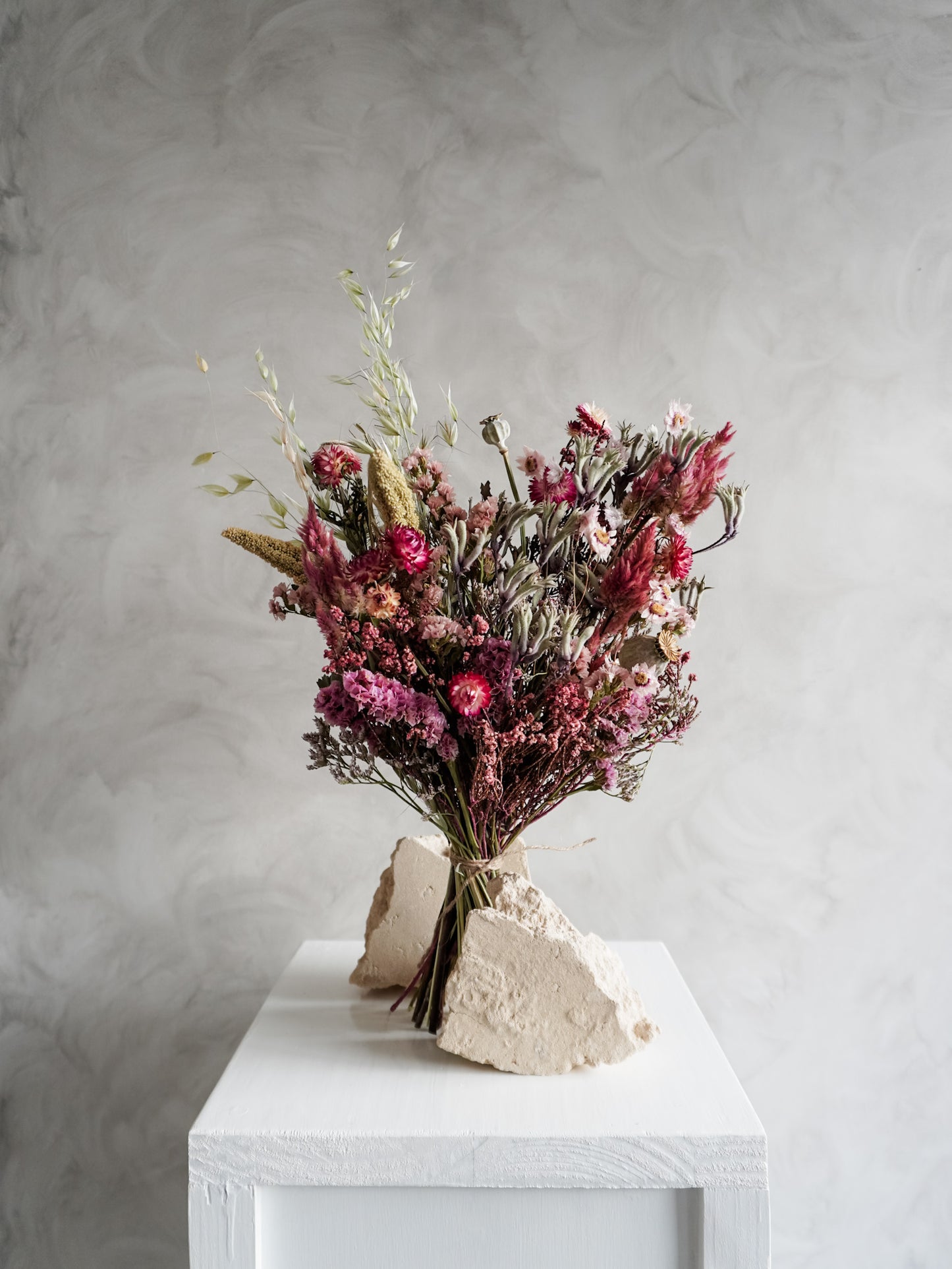 Bouquet of colourful dried flowers on a white plinth against a grey background - classic size distant view.