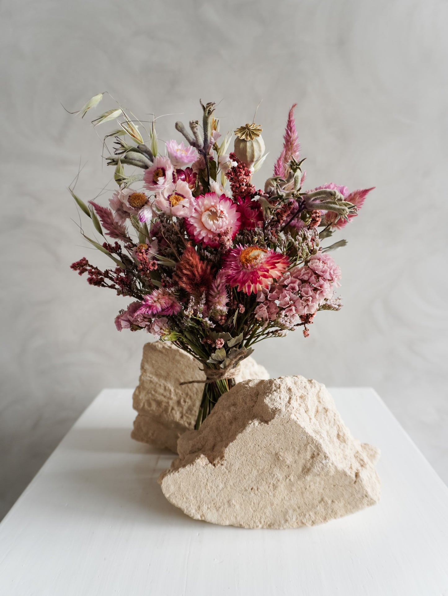 Bouquet of colourful dried flowers on a white plinth against a grey background - posy size close view.