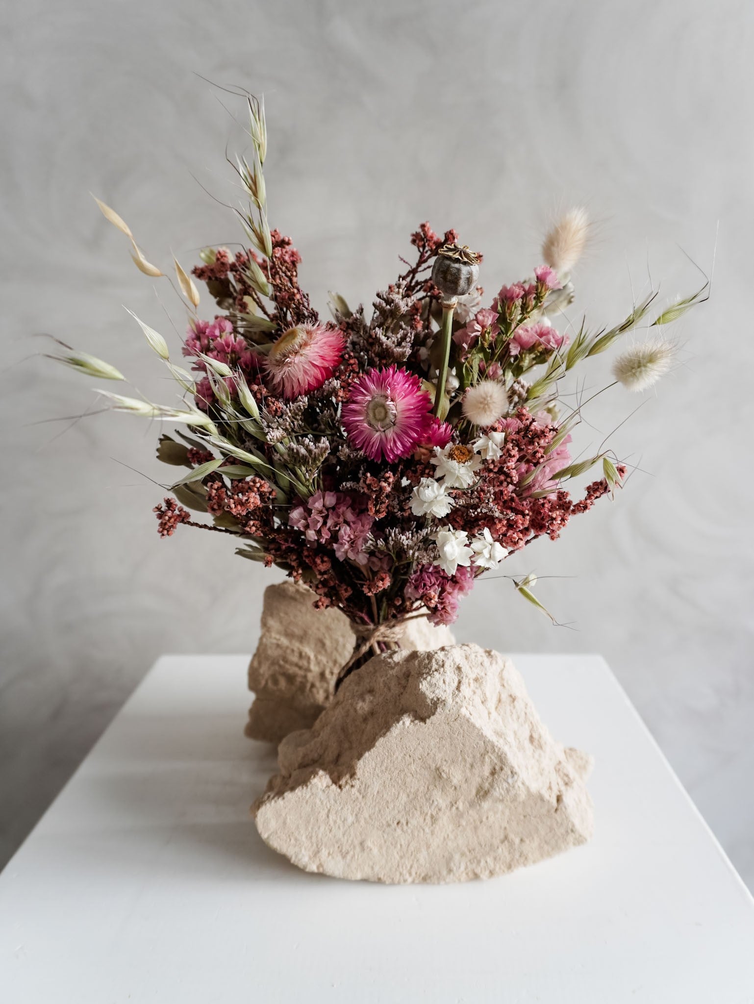 Dried flower bouquet in vibrant colours on a white plinth against a gray background - Posy Size close view.