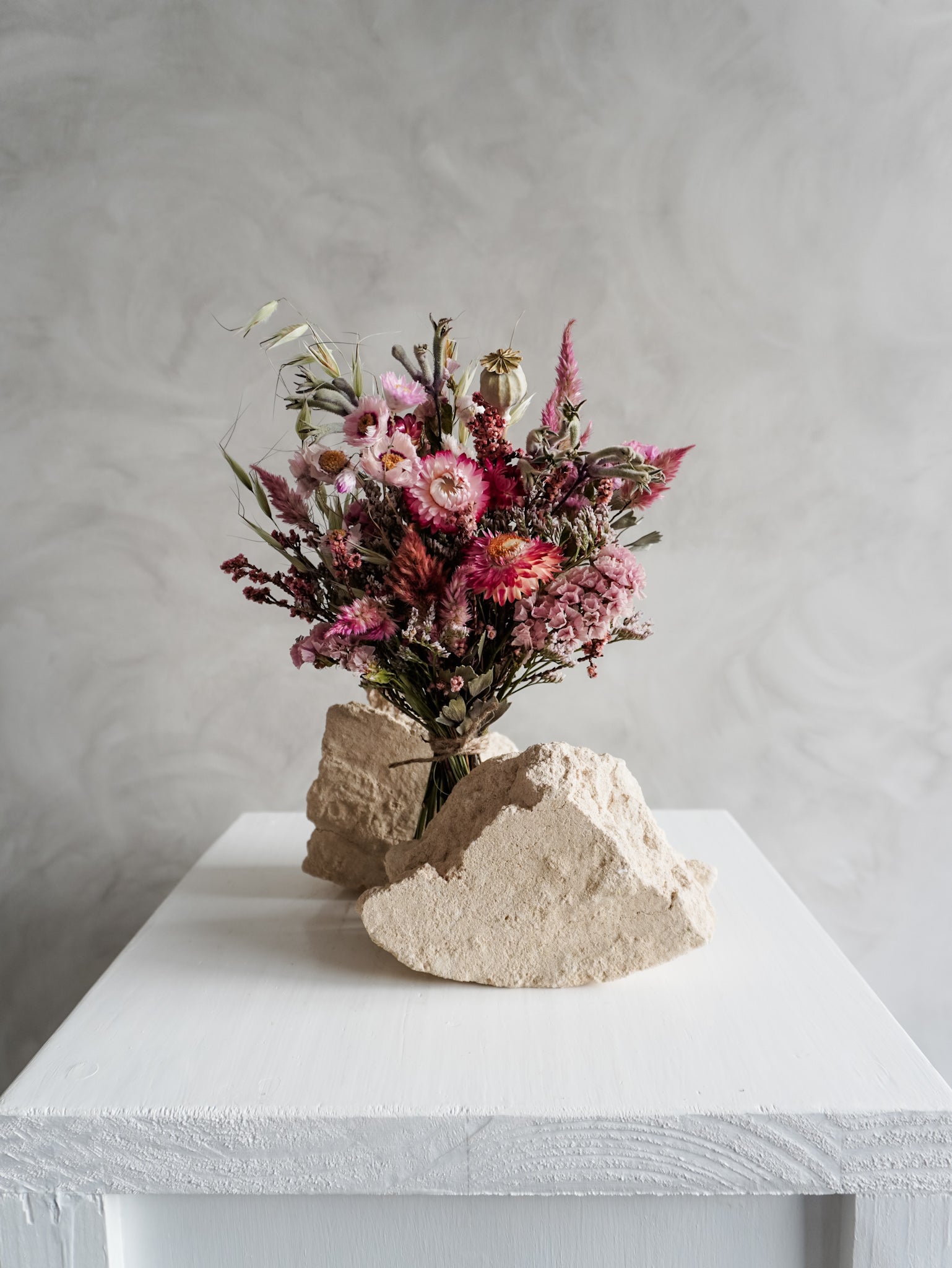 Bouquet of colourful dried flowers on a white plinth against a grey background - posy size distant view.