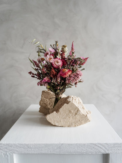 Bouquet of colourful dried flowers on a white plinth against a grey background - posy size distant view.