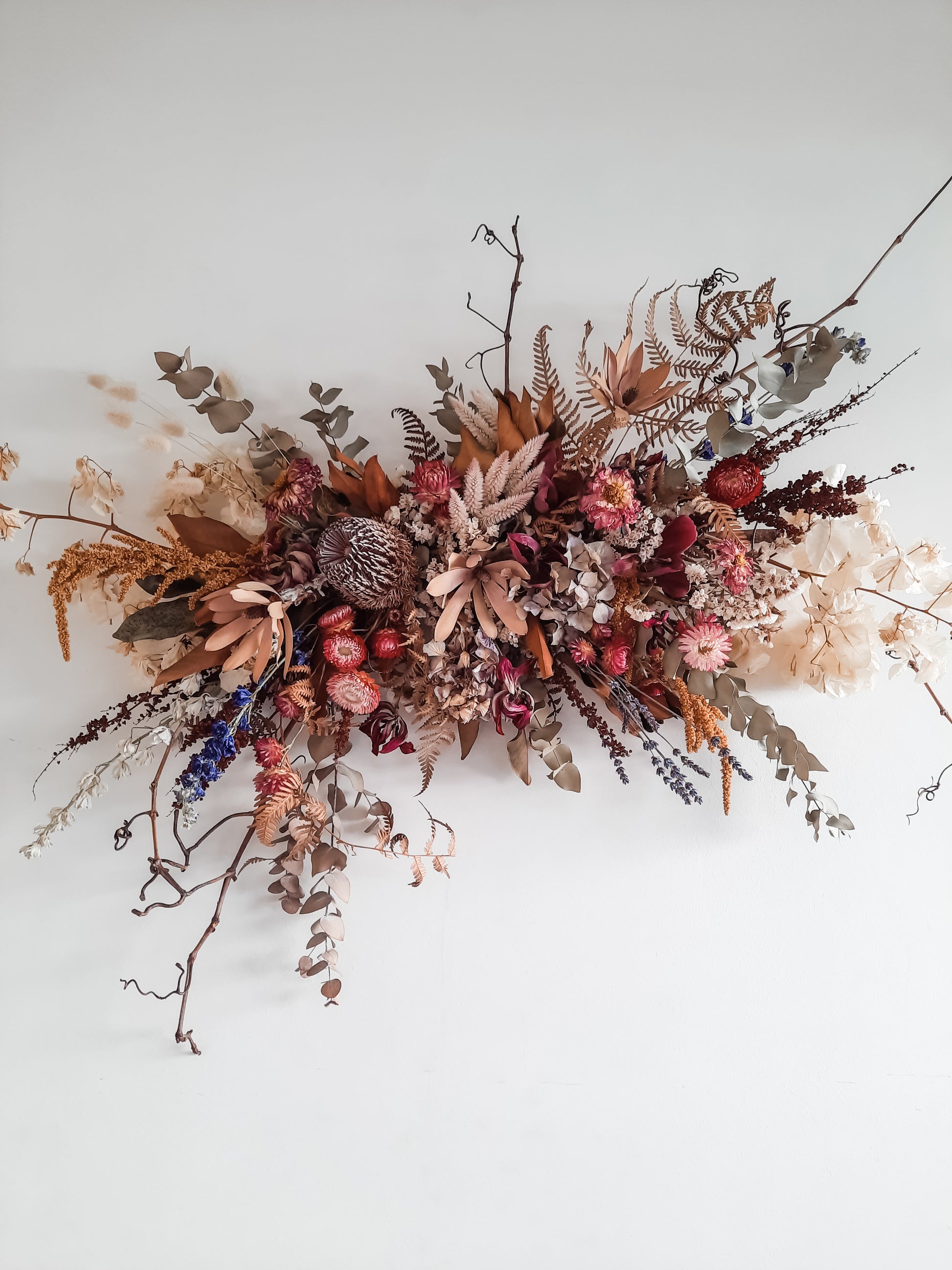 Dried flower wall hanging in berry tones.