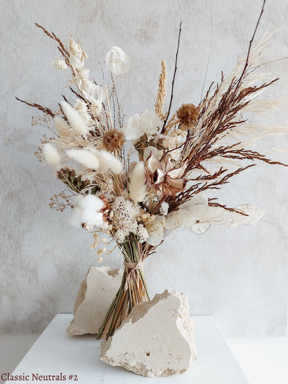 A dried flower bouquet featuring white, cream, and earthy flowers against a textured light gray background.