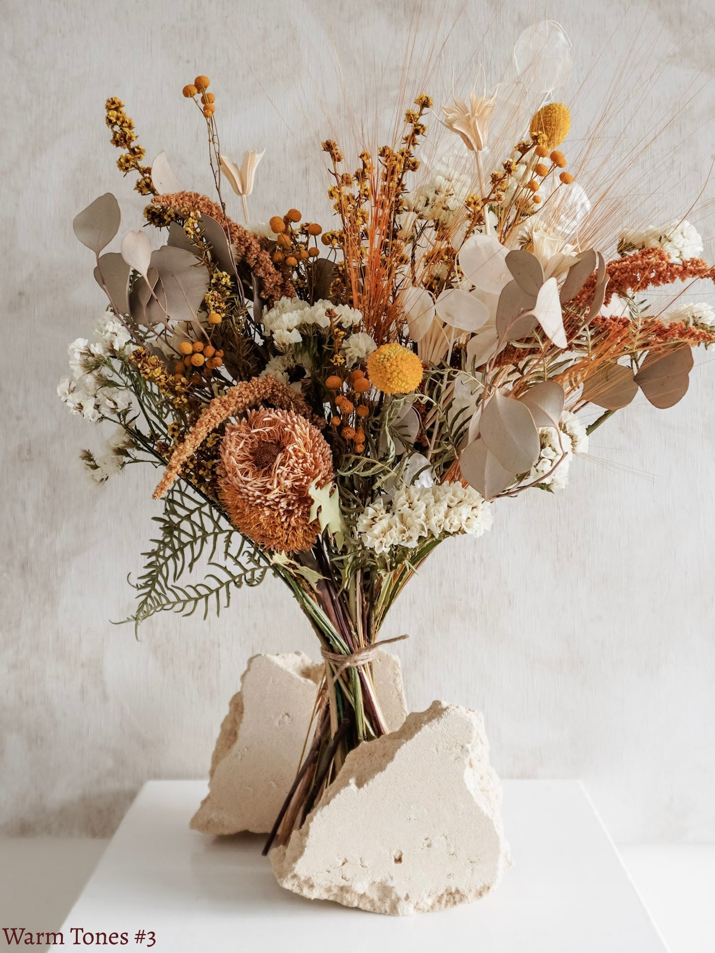 A dried flower bouquet featuring yellow, orange, and white flowers against a textured light gray background.