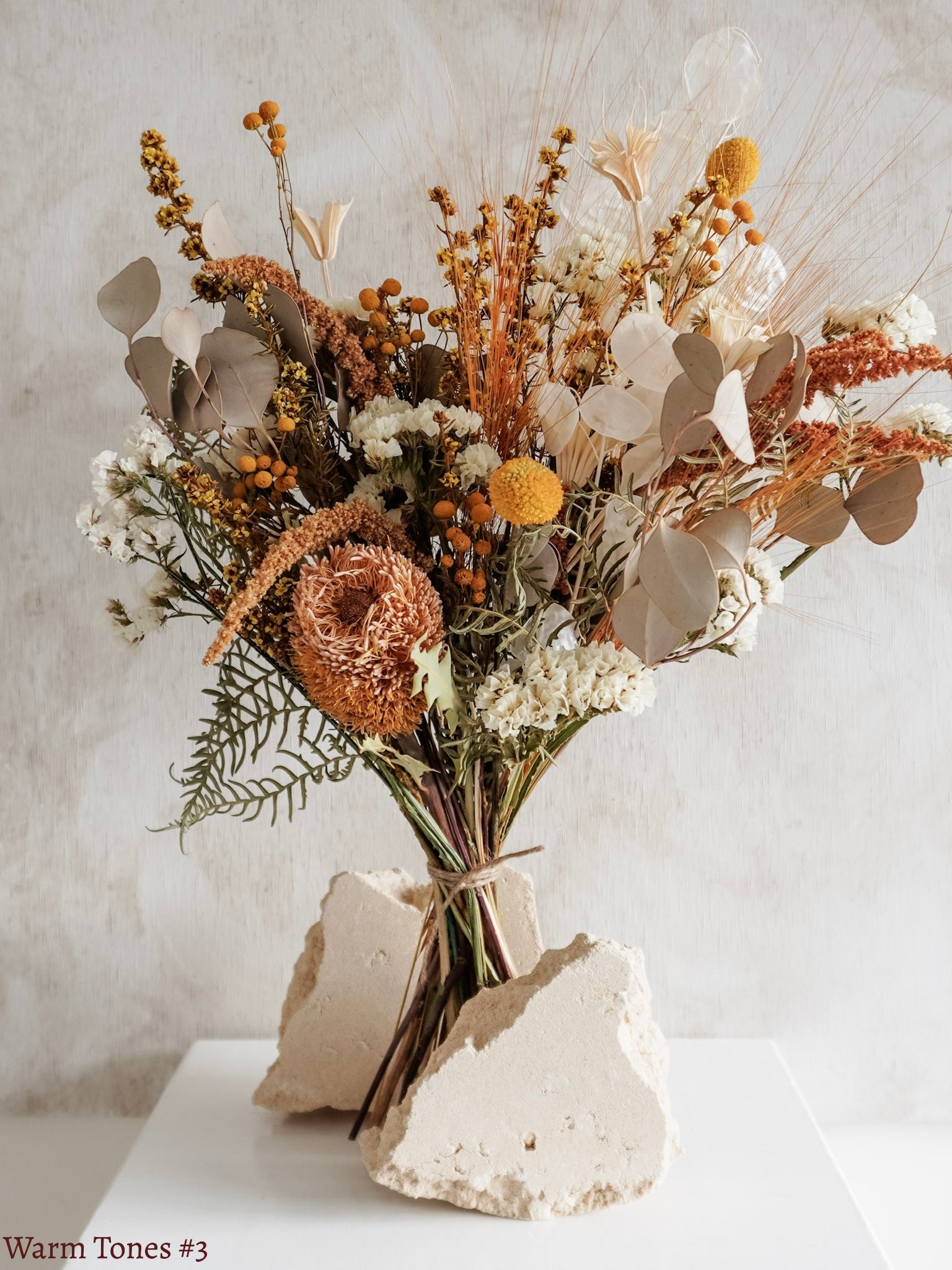 A dried flower bouquet featuring yellow, orange, and white flowers against a textured light gray background.