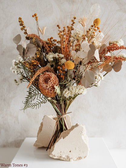 A dried flower bouquet featuring yellow, orange, and white flowers against a textured light gray background.