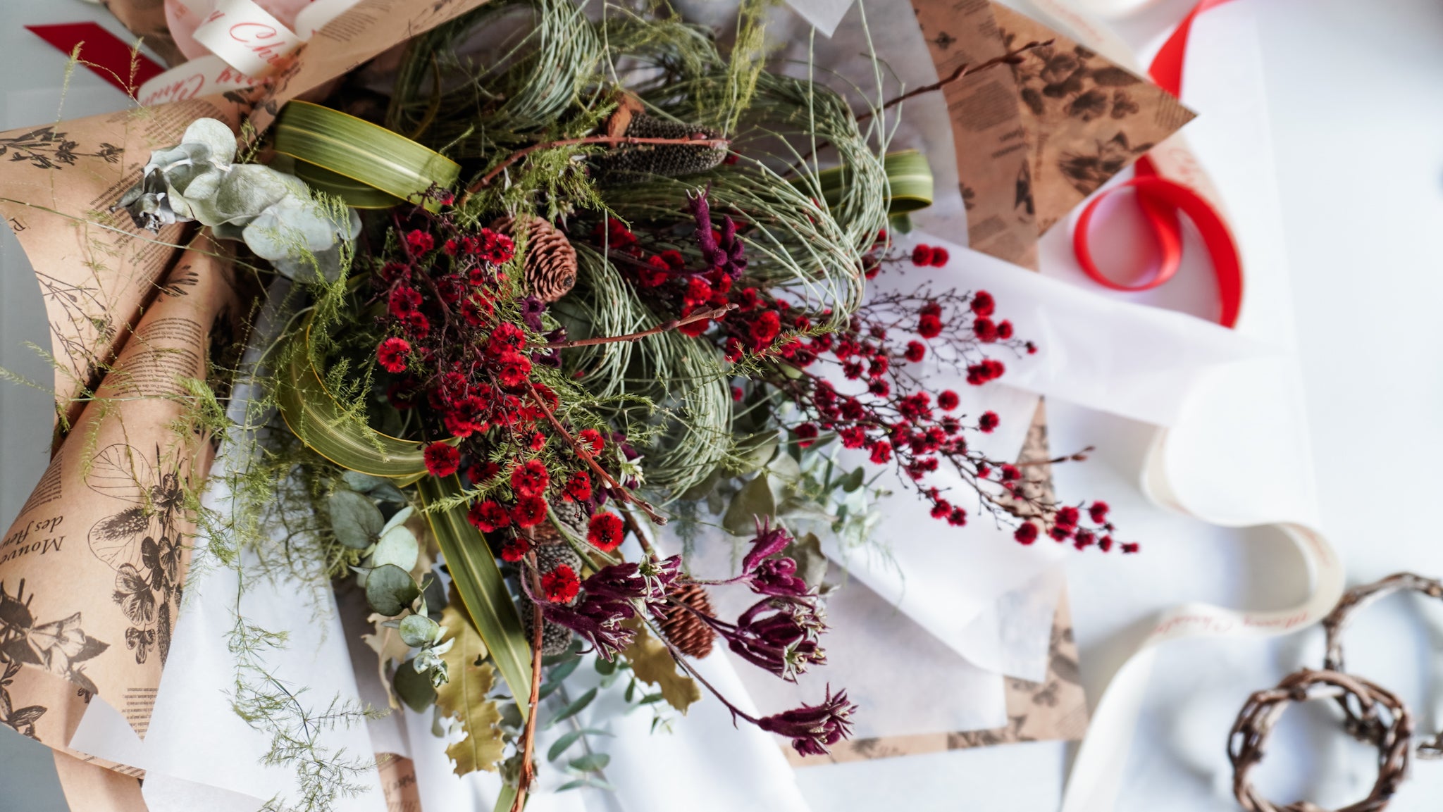 Dried flower bouquet in Christmas green and red tones wrapped in white tissue and brown paper.